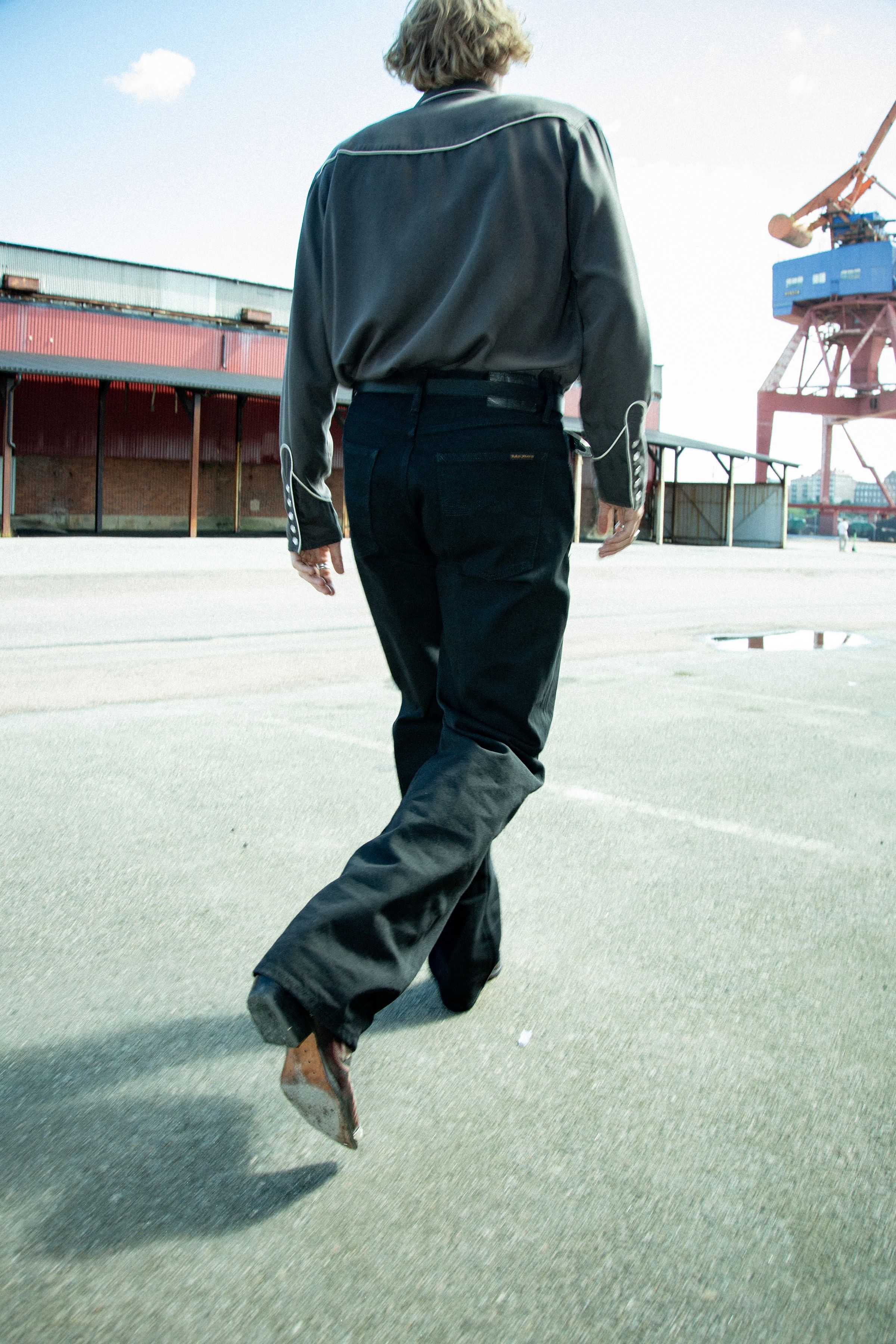 Nudie Jeans Tuff Tony in Black Water, a men's loose fit jean worn by a model and shown from the back as he walks.