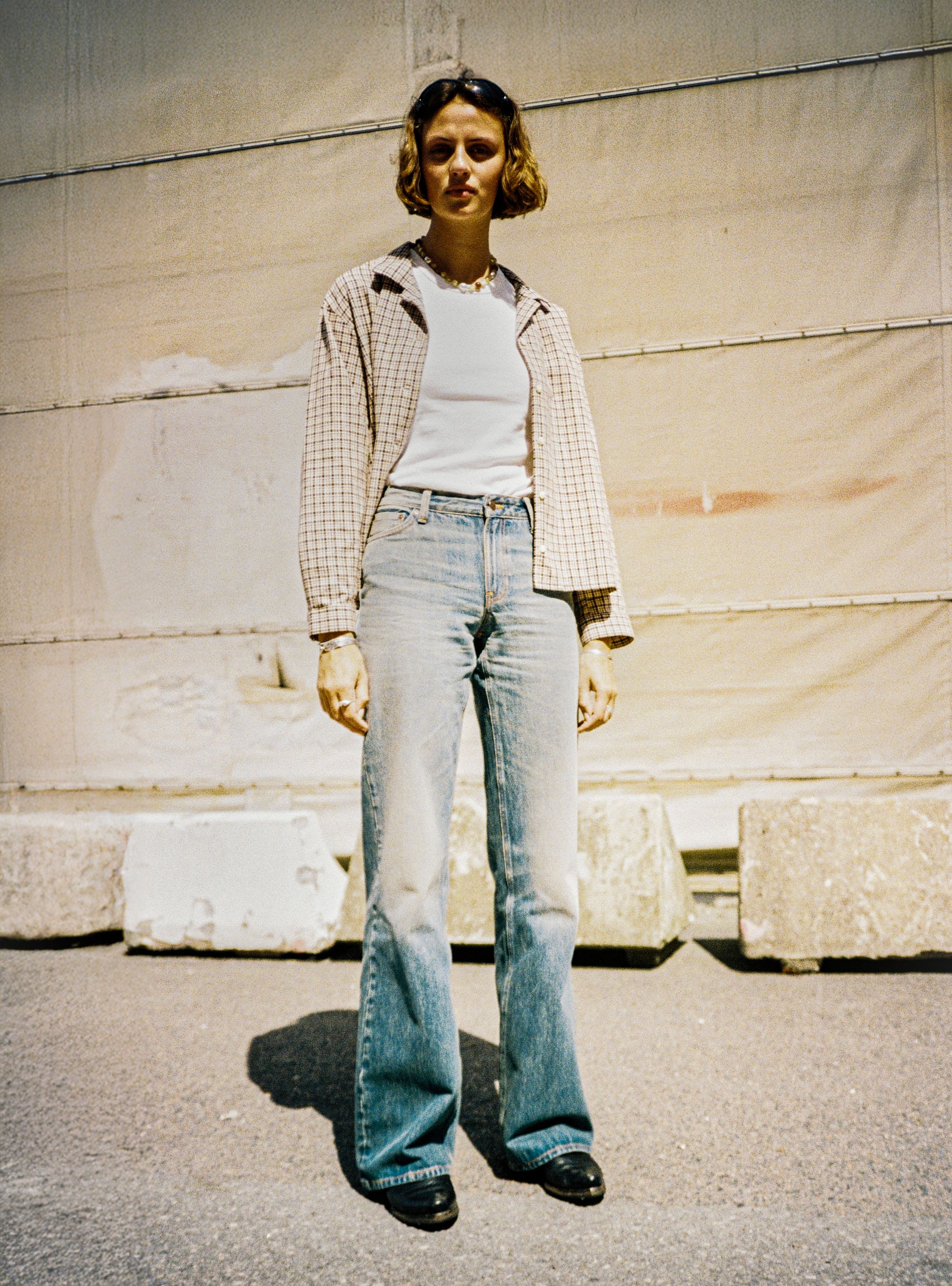 Nudie Jeans Juni Checked Shirt in Brown, a women's shirt worn open over a t-shirt by a model standing outdoors.