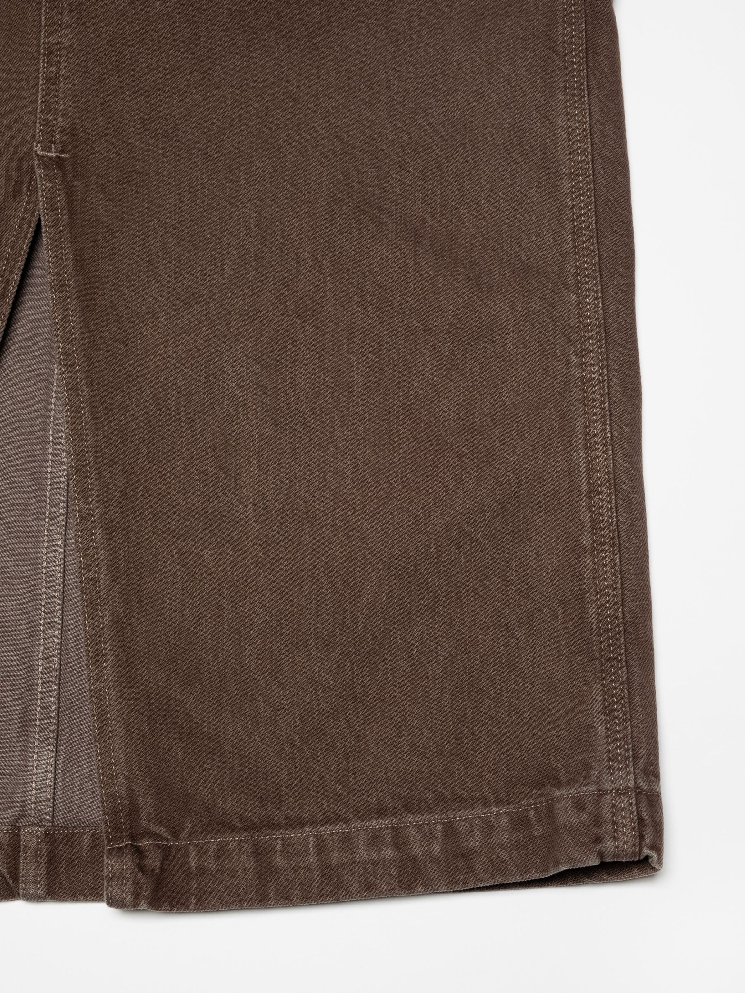 Nudie Jeans Inger Dungarees Dress Espresso, a women's dungaree dress, shown in a close-up of the front slit and hem detail.