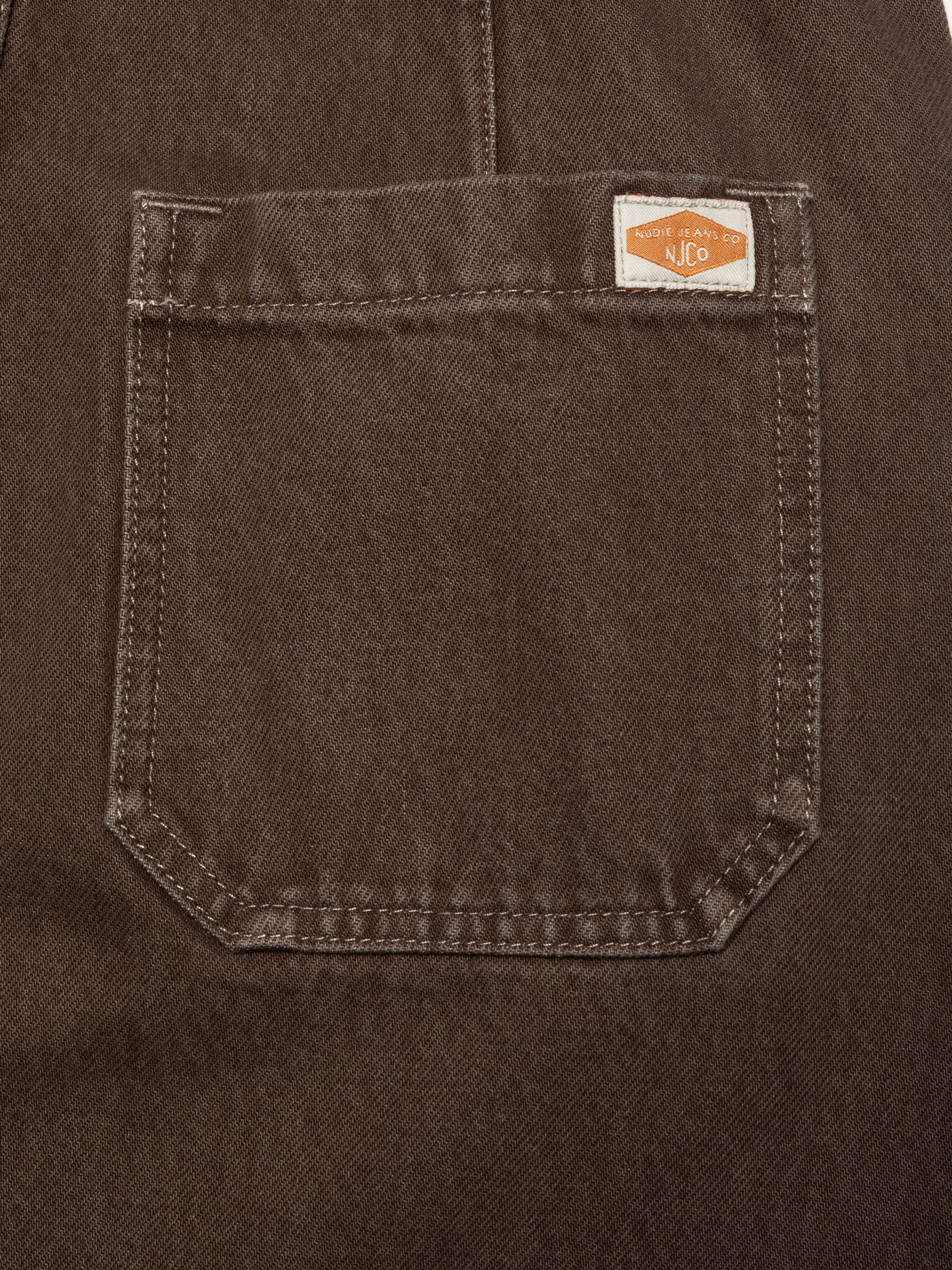 Nudie Jeans Inger Dungarees Dress Espresso, a women's dress in brown denim, showing a close-up of the back pocket.