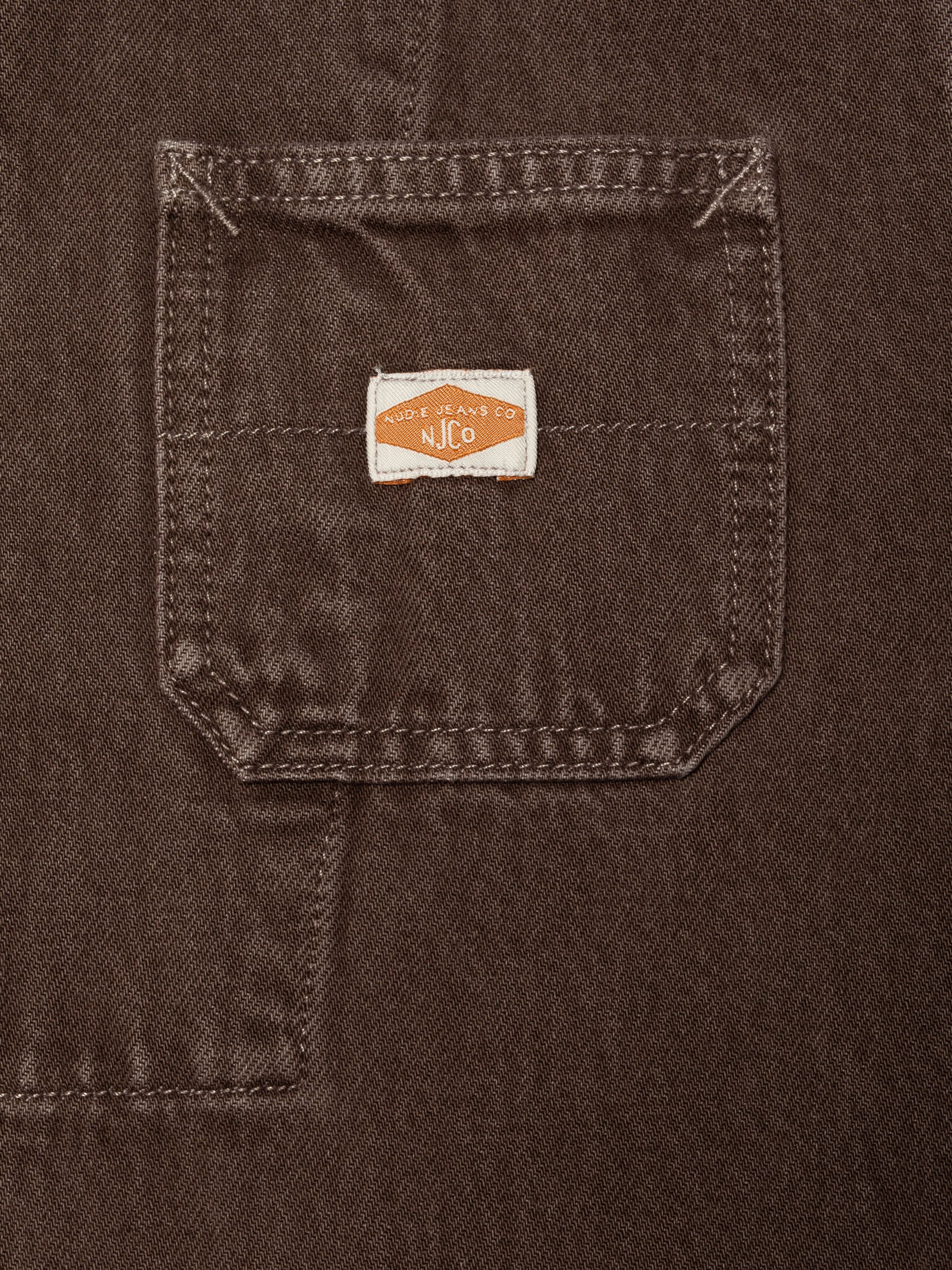 Nudie Jeans Ada Workwear Jacket Espresso, a close-up detail shot of the patch pocket with the woven brand label.