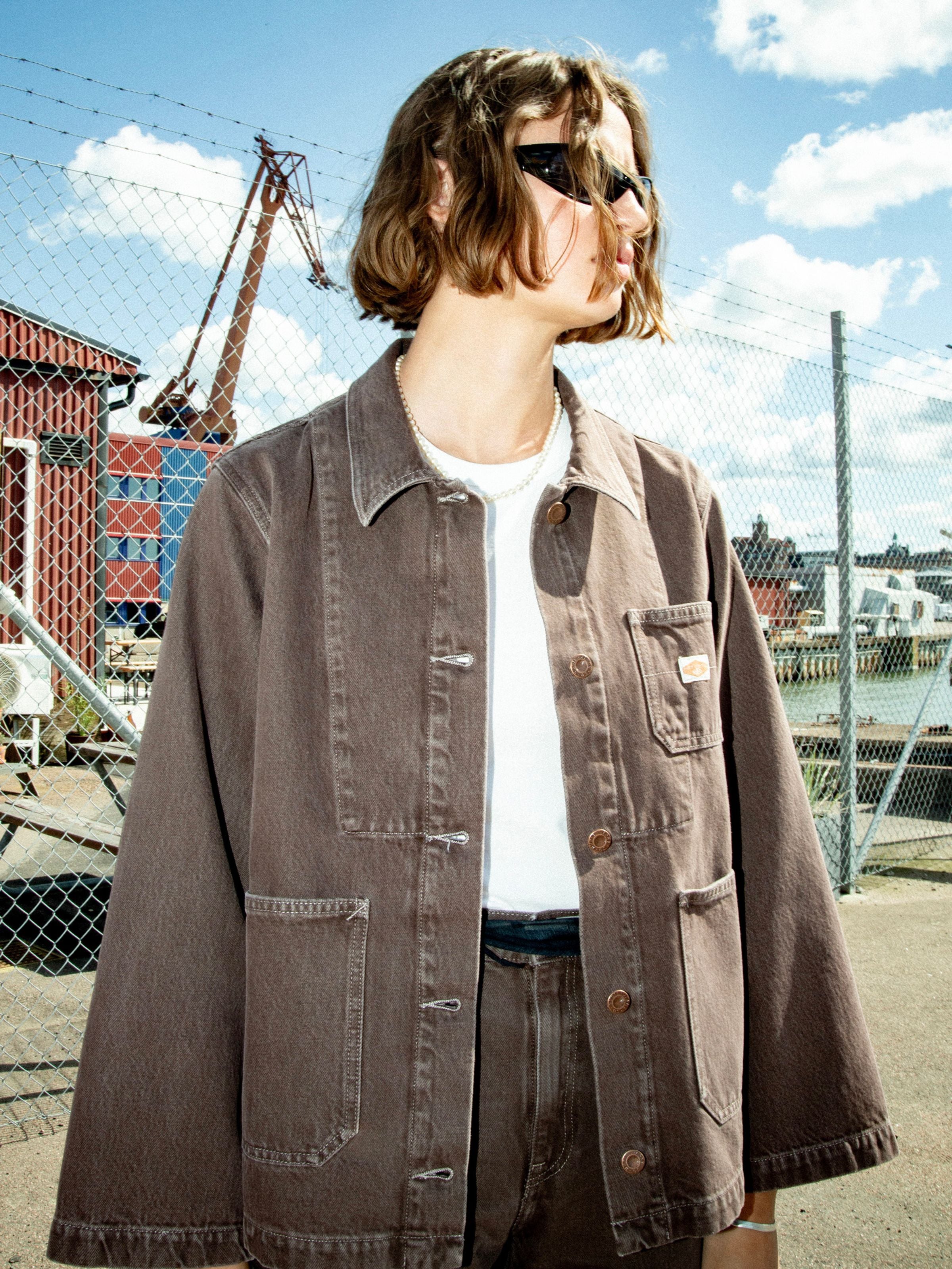 Nudie Jeans Ada Workwear Jacket Espresso, eine braune Damen-Workwear-Jacke, von einem Model im Freien getragen.