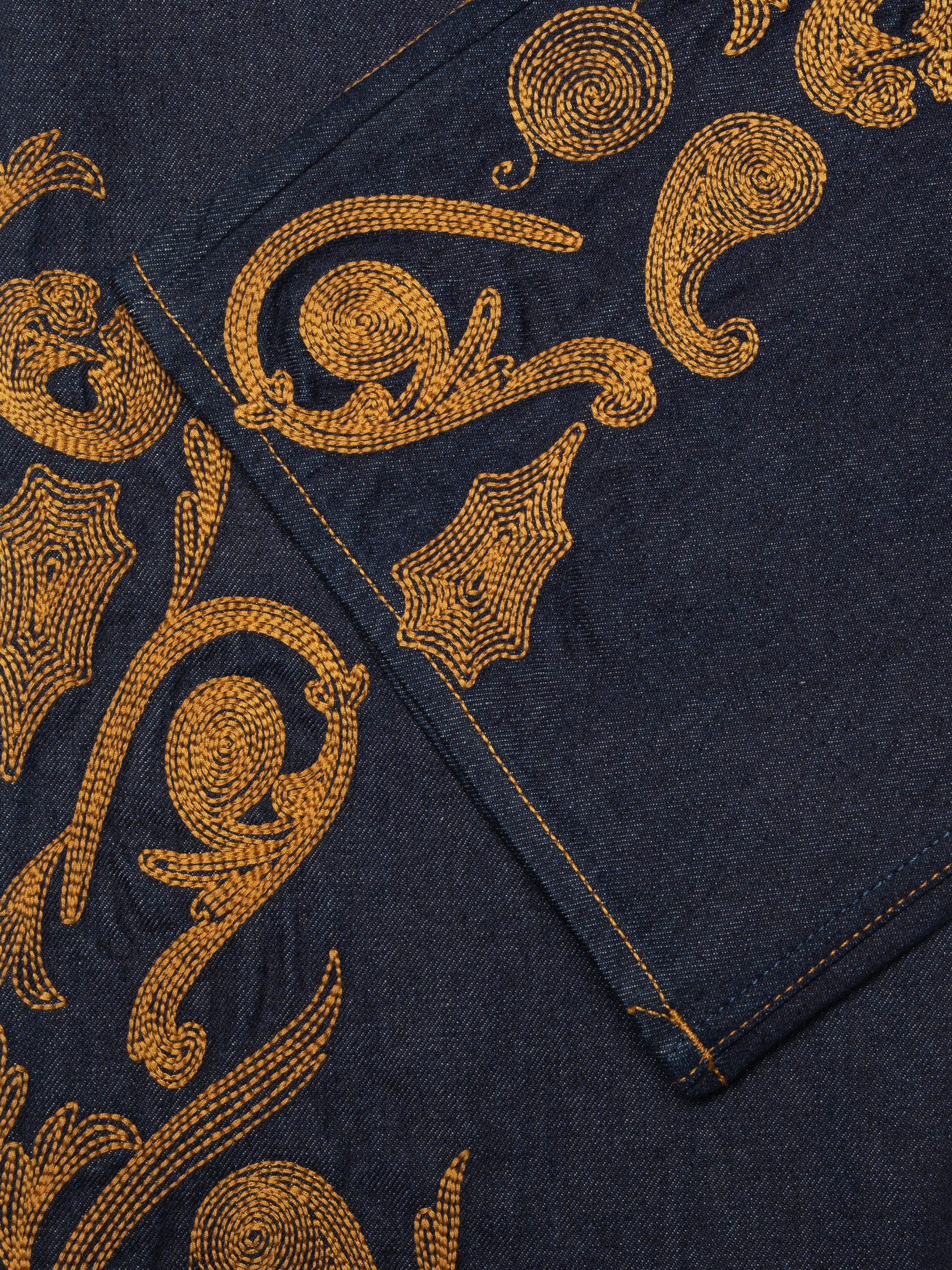 Nudie Jeans Holly Western Pants in mid-blue denim, showing a close-up of the intricate tobacco western embroidery.