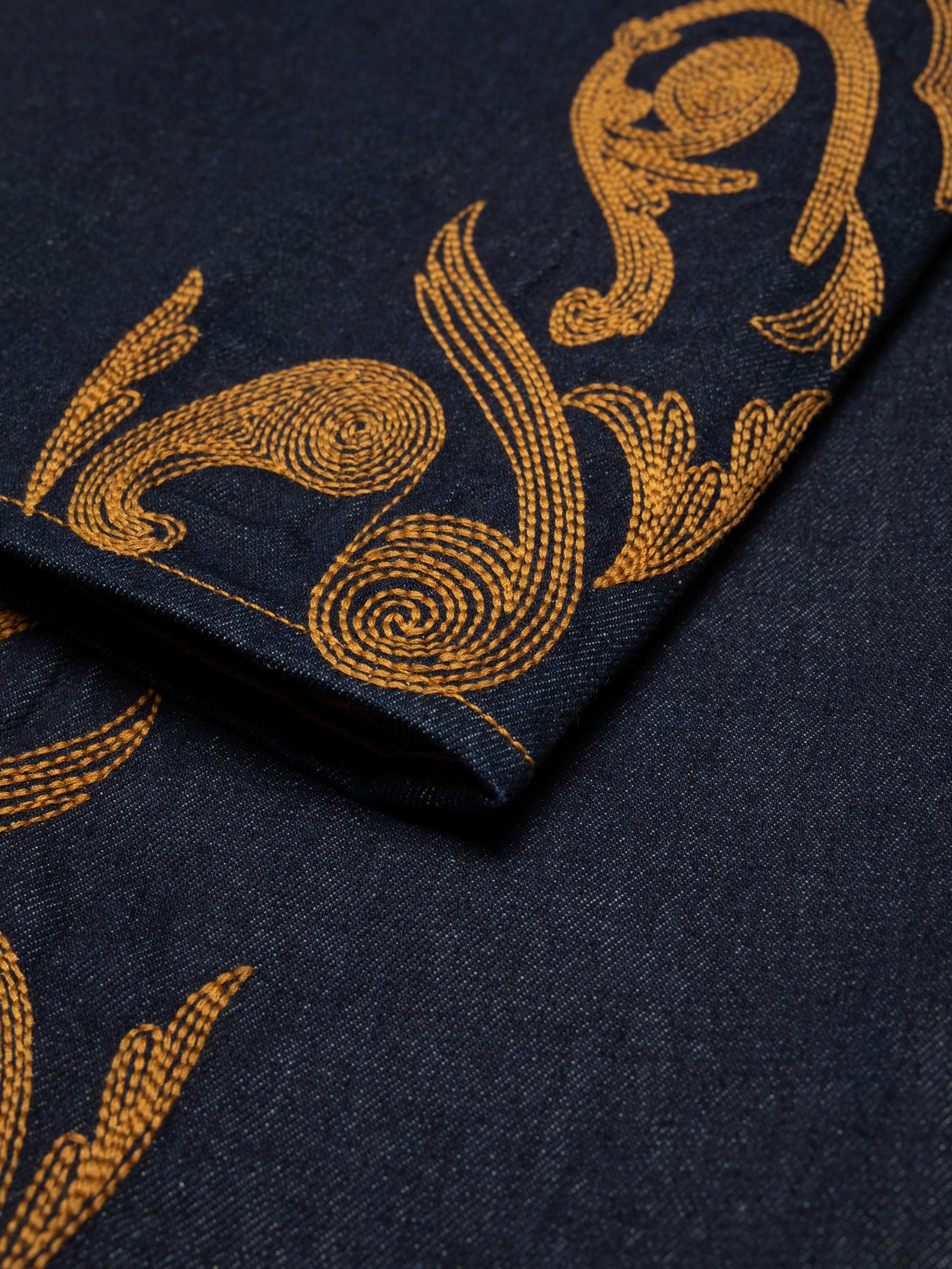 Nudie Jeans Holly Western Pants Embroidery, a close-up of the intricate tobacco-colored embroidery on dark blue denim.
