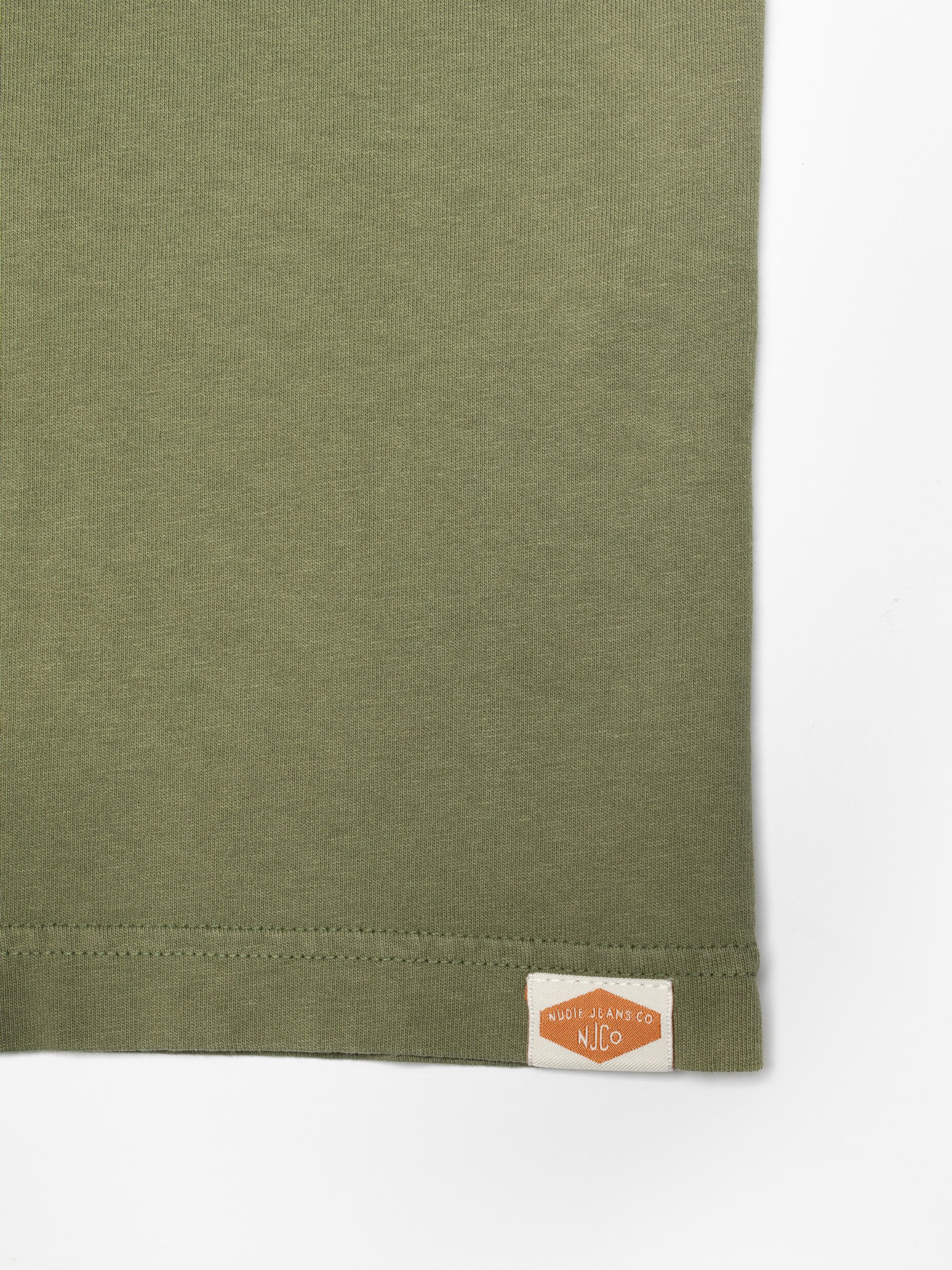 Nudie Jeans Uno Everyday T-Shirt in Green, close-up of the hem showing the woven Nudie Jeans Co logo tab.