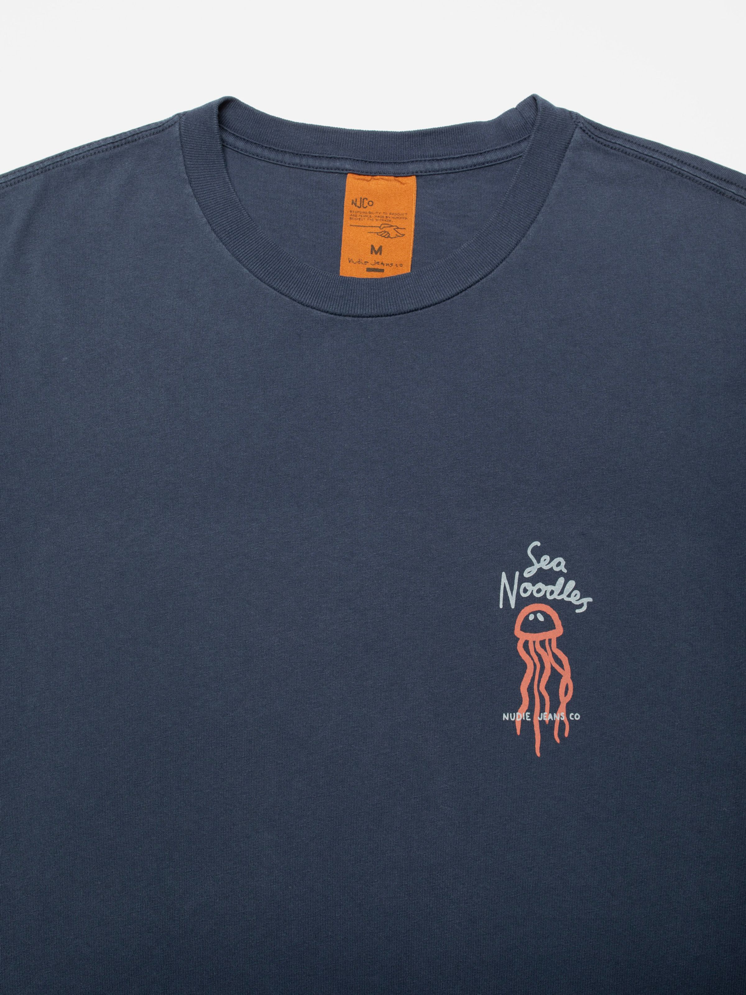Nudie Jeans Roy Sea Noodles T-Shirt in dark blue, showing a close-up of the chest print and collar area.