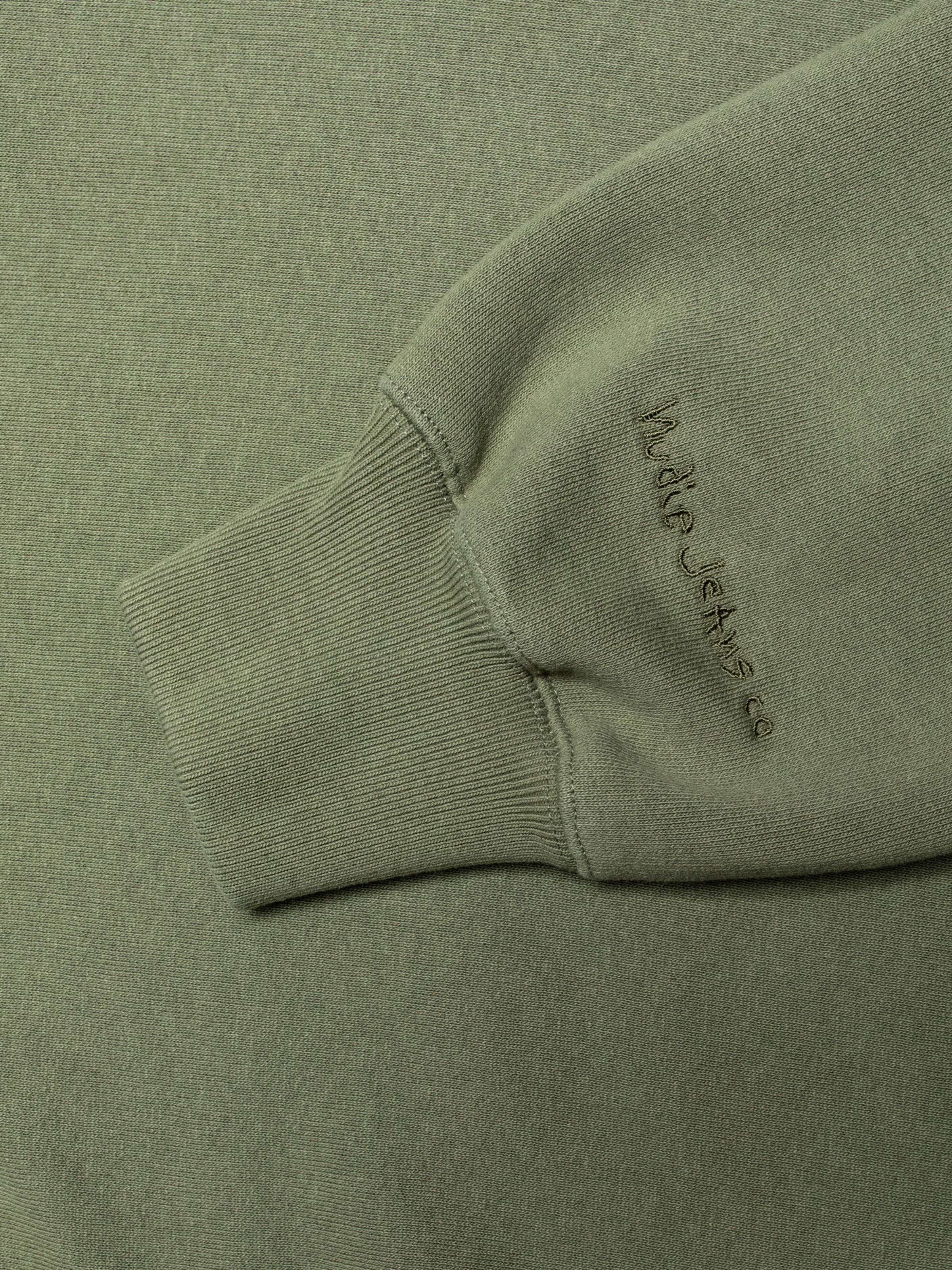 Nudie Jeans Hasse Crew Neck Sweatshirt in green, close-up detail of the sleeve cuff and tonal logo embroidery.