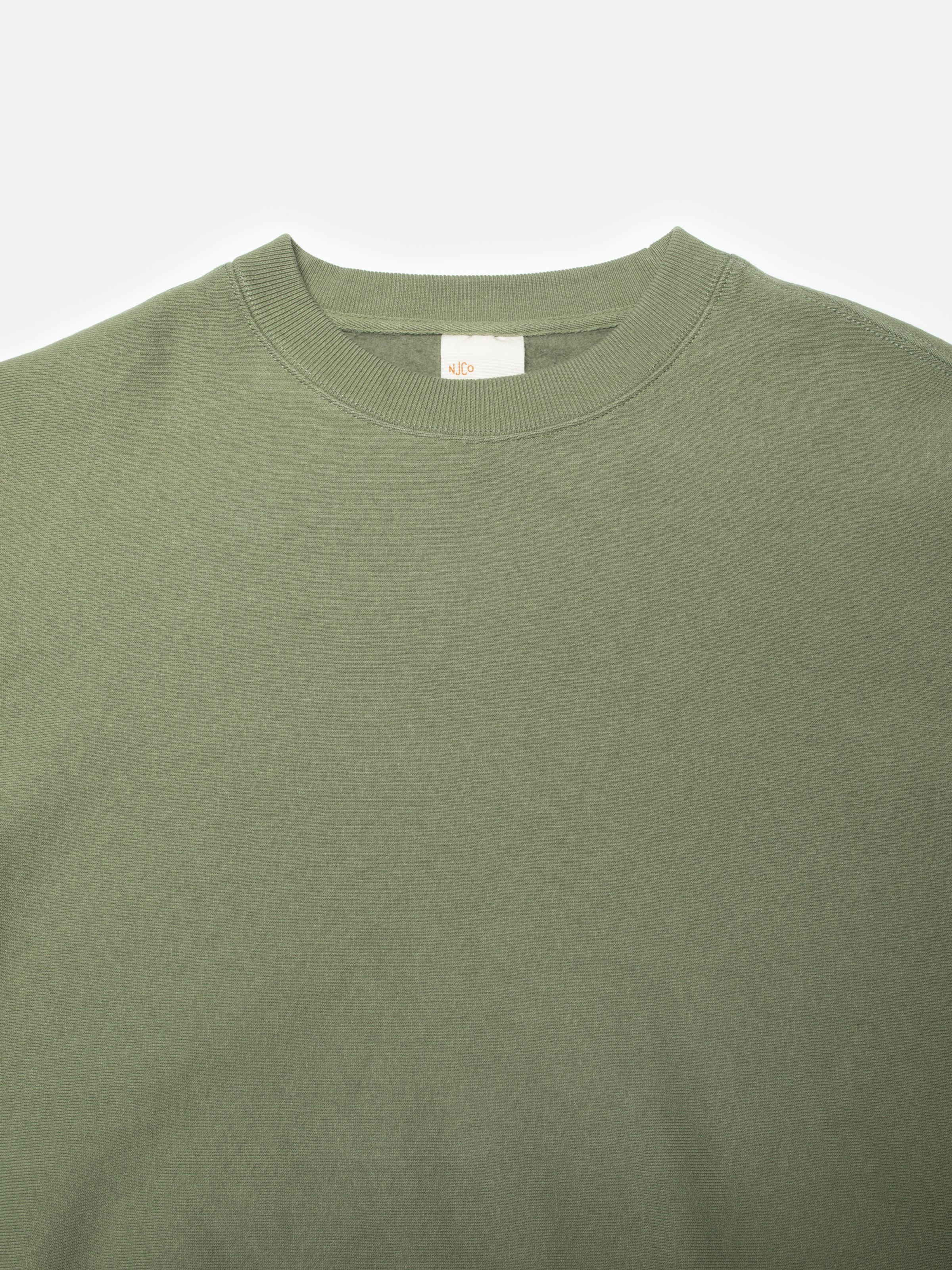 Nudie Jeans Hasse Crew Neck Sweatshirt in green, a close-up of the ribbed crew neck and interior brand label.