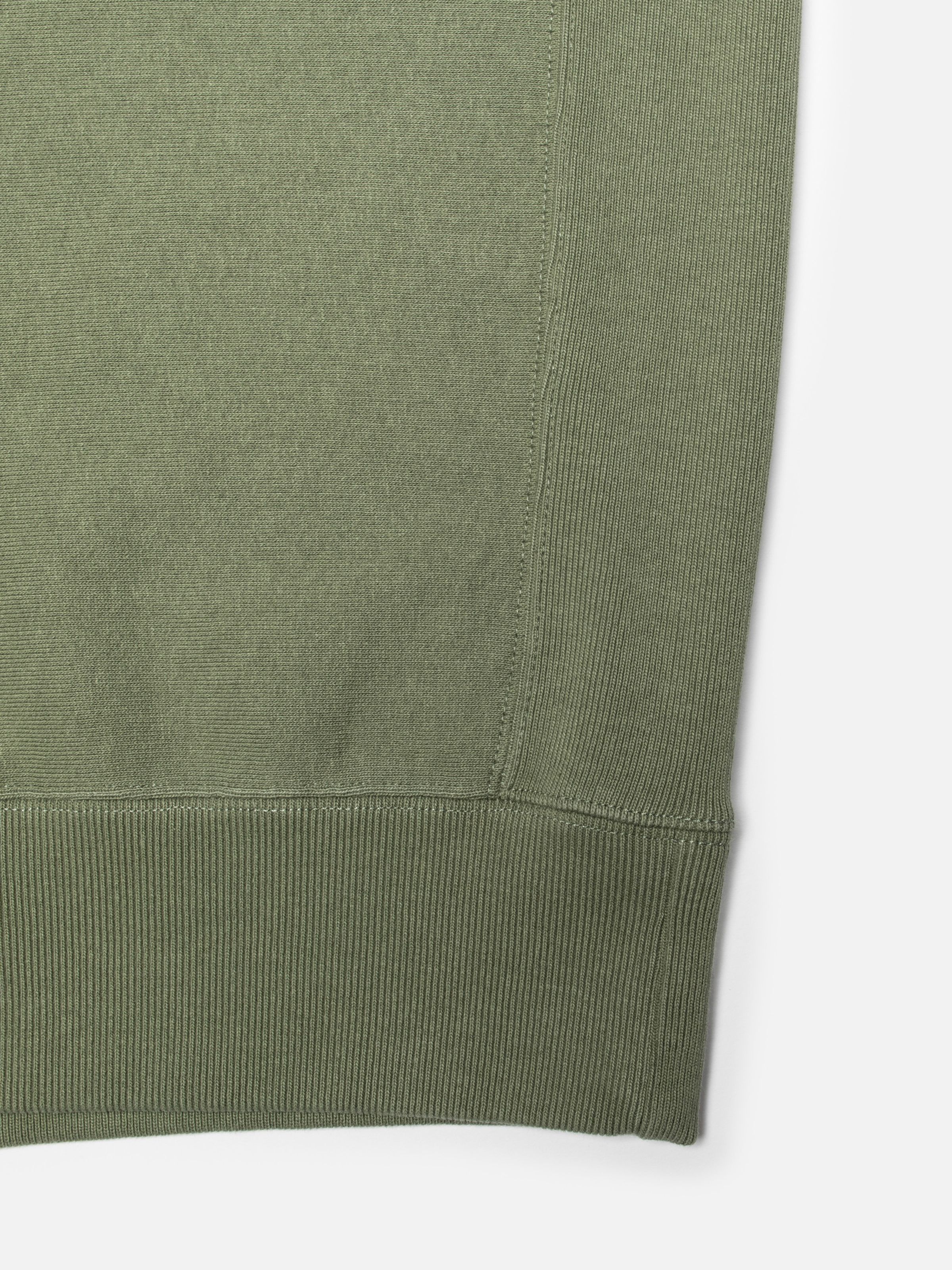 Nudie Jeans Hasse Crew Neck Sweatshirt in Green, close-up of the ribbed hem and side seam insert.