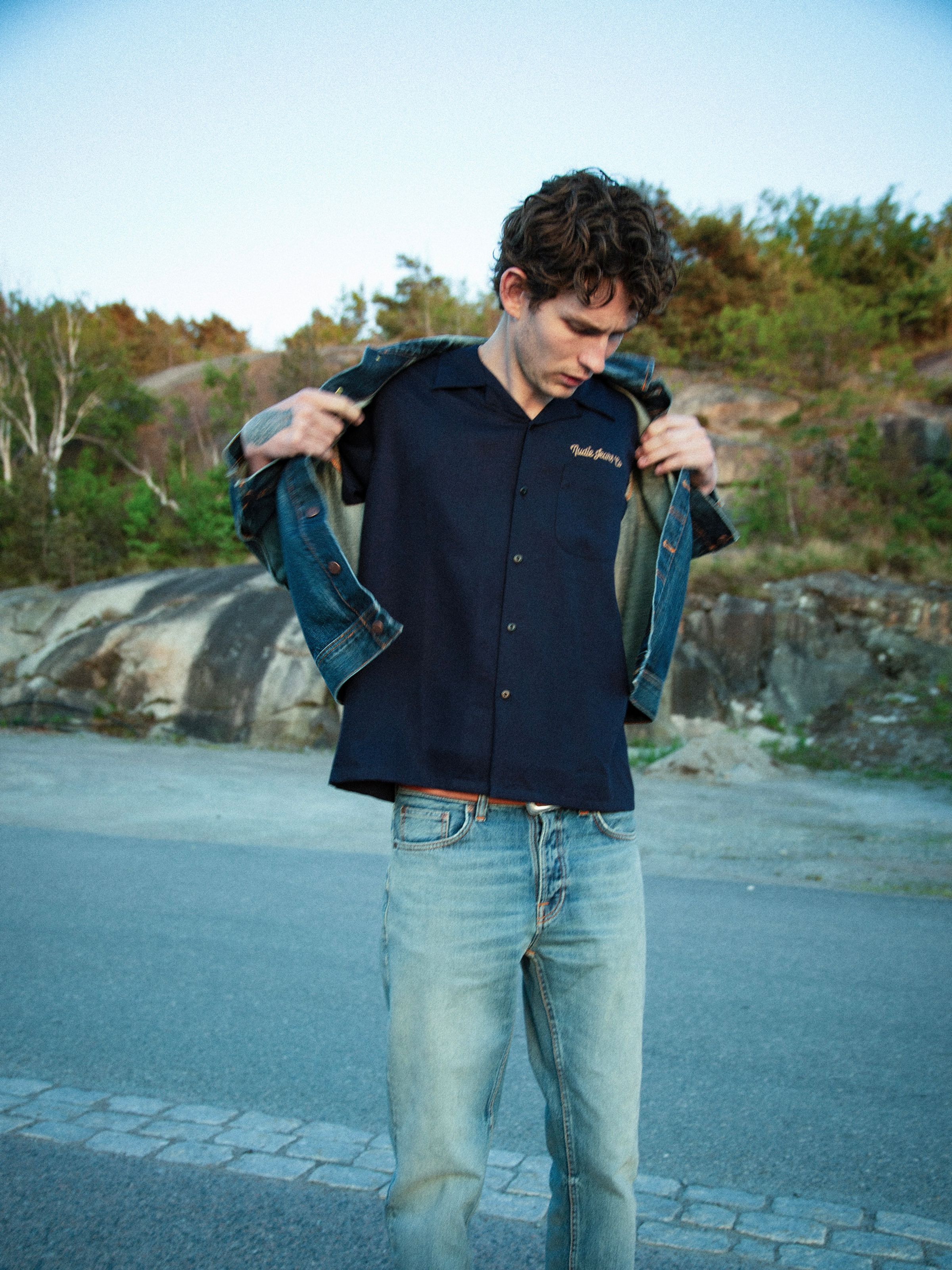 Nudie Jeans Arthur Bowling Shirt 8 Wonders, men's navy bowling shirt shown on a model outdoors with a denim jacket.