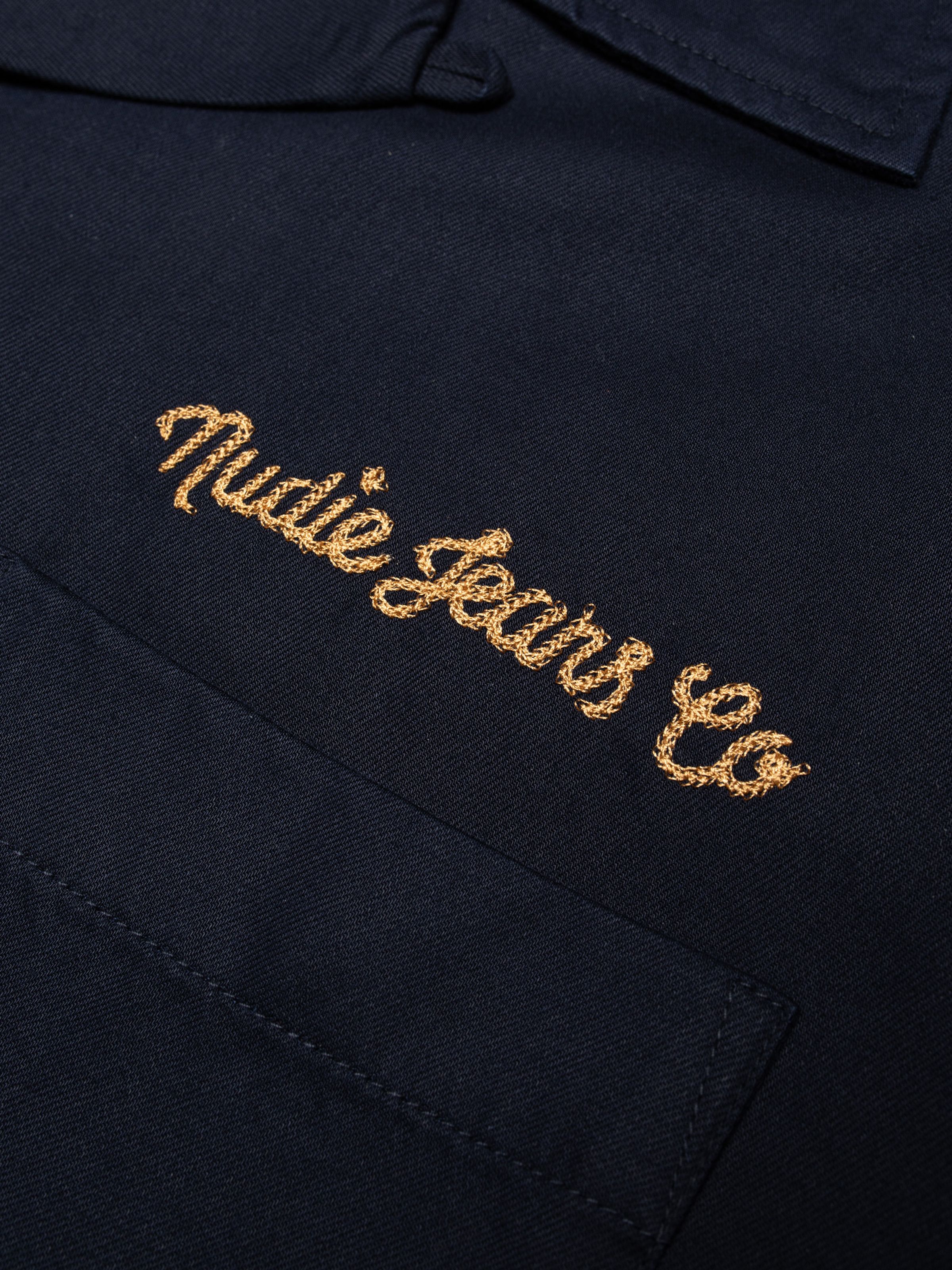 Nudie Jeans Arthur Bowling Shirt 8 Wonders in Navy, close-up of the chain stitch logo embroidery on the chest.