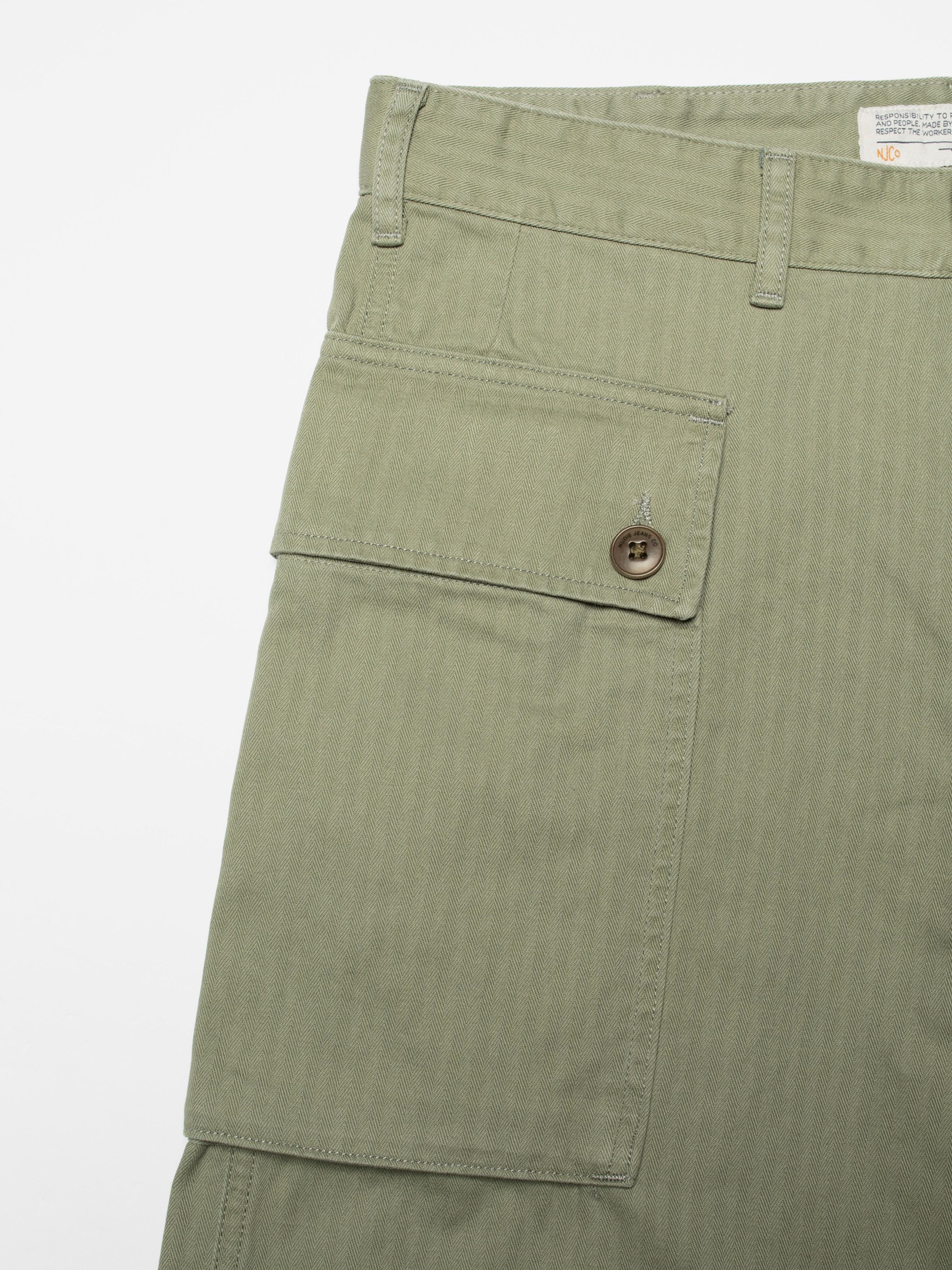 Nudie Jeans Loud Larry Pants Pale Green, men's loose fit pants. Close-up of the side cargo pocket and herringbone fabric.