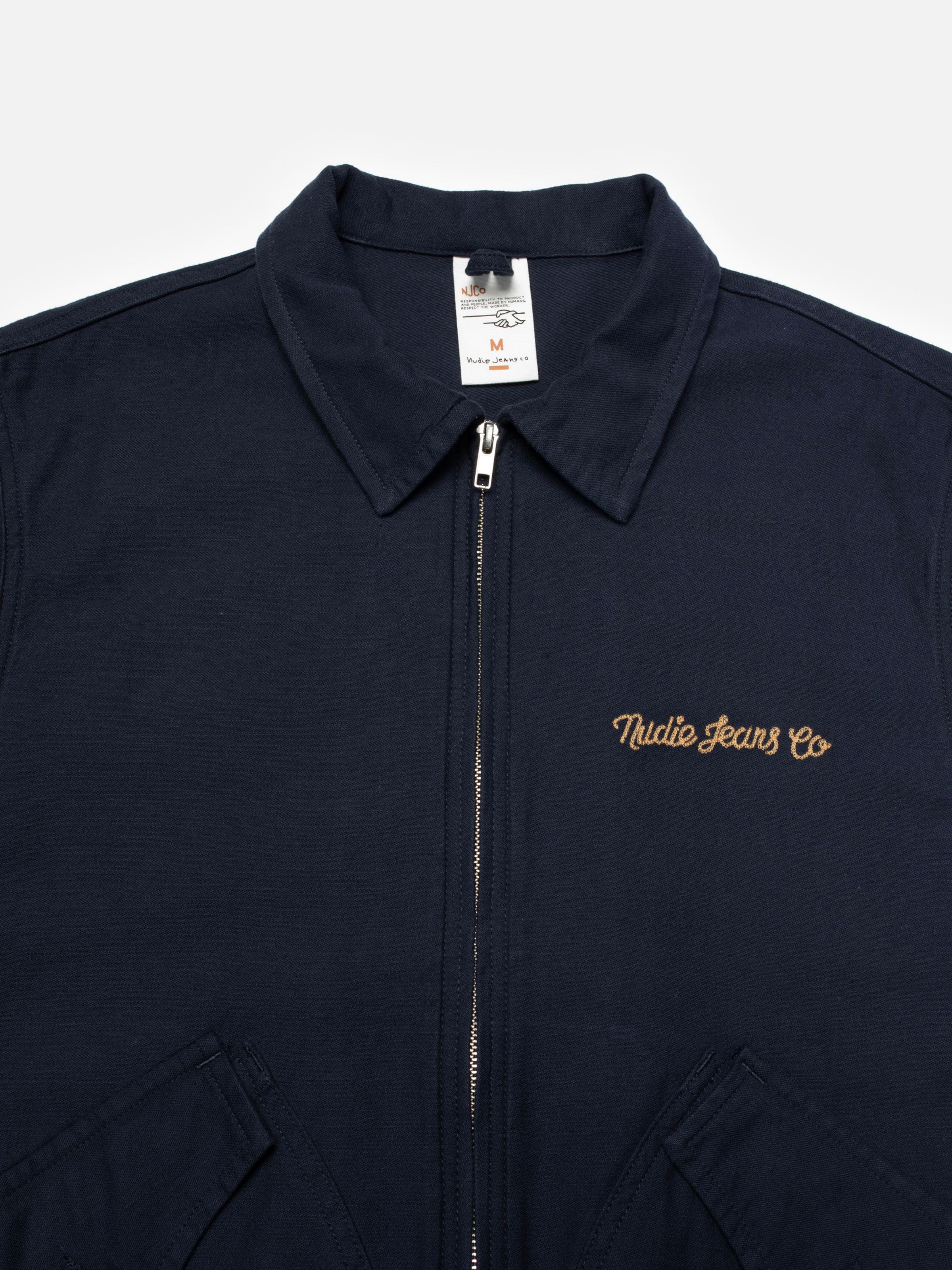 Nudie Jeans Blake Zip Jacket Back Sateen in Navy, close-up of the chest showing the embroidered logo and zipper.