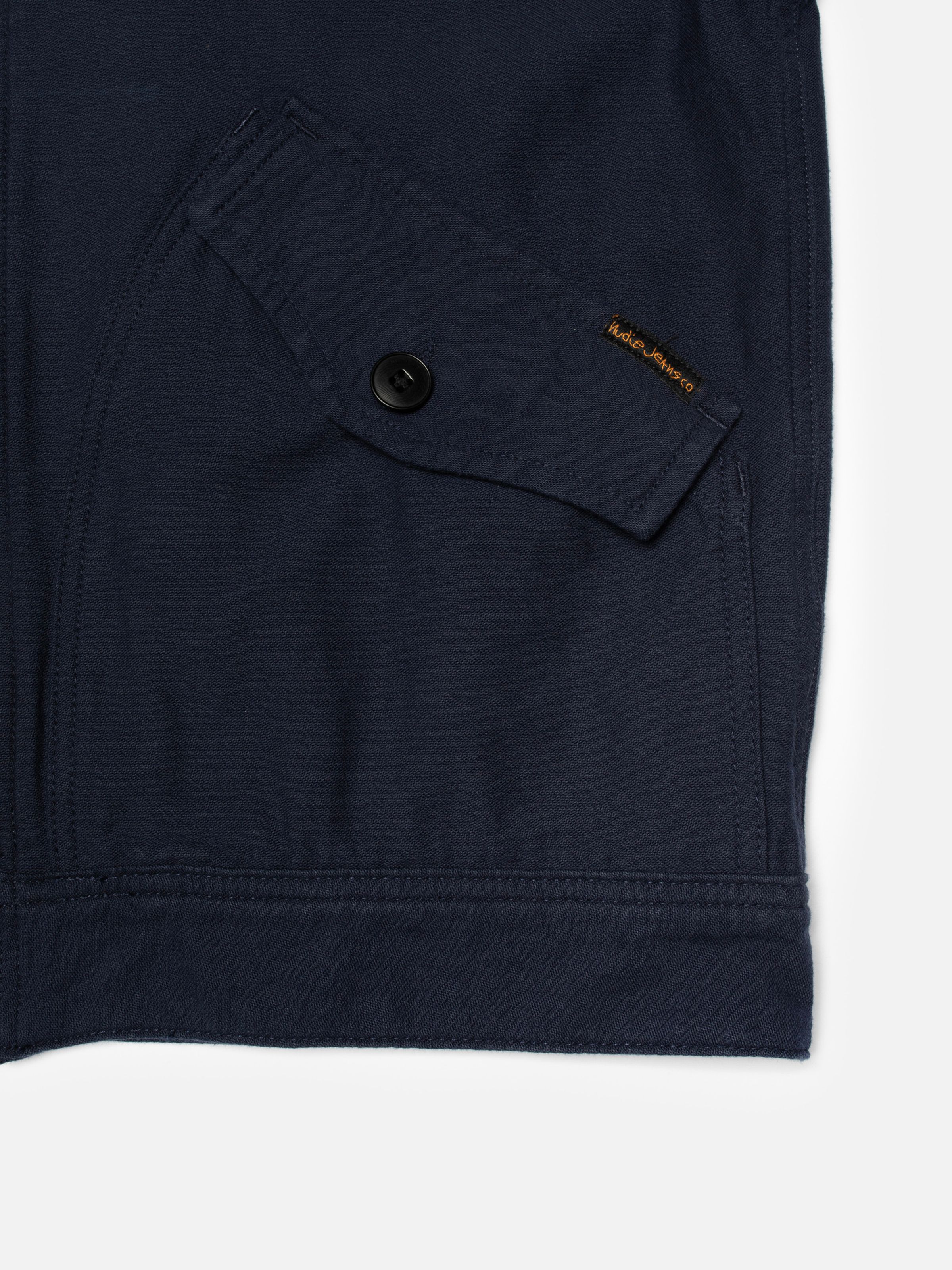 Nudie Jeans Blake Zip Jacket Back Sateen in Navy, close-up of a back pocket detail showing the buttoned flap and logo tab.