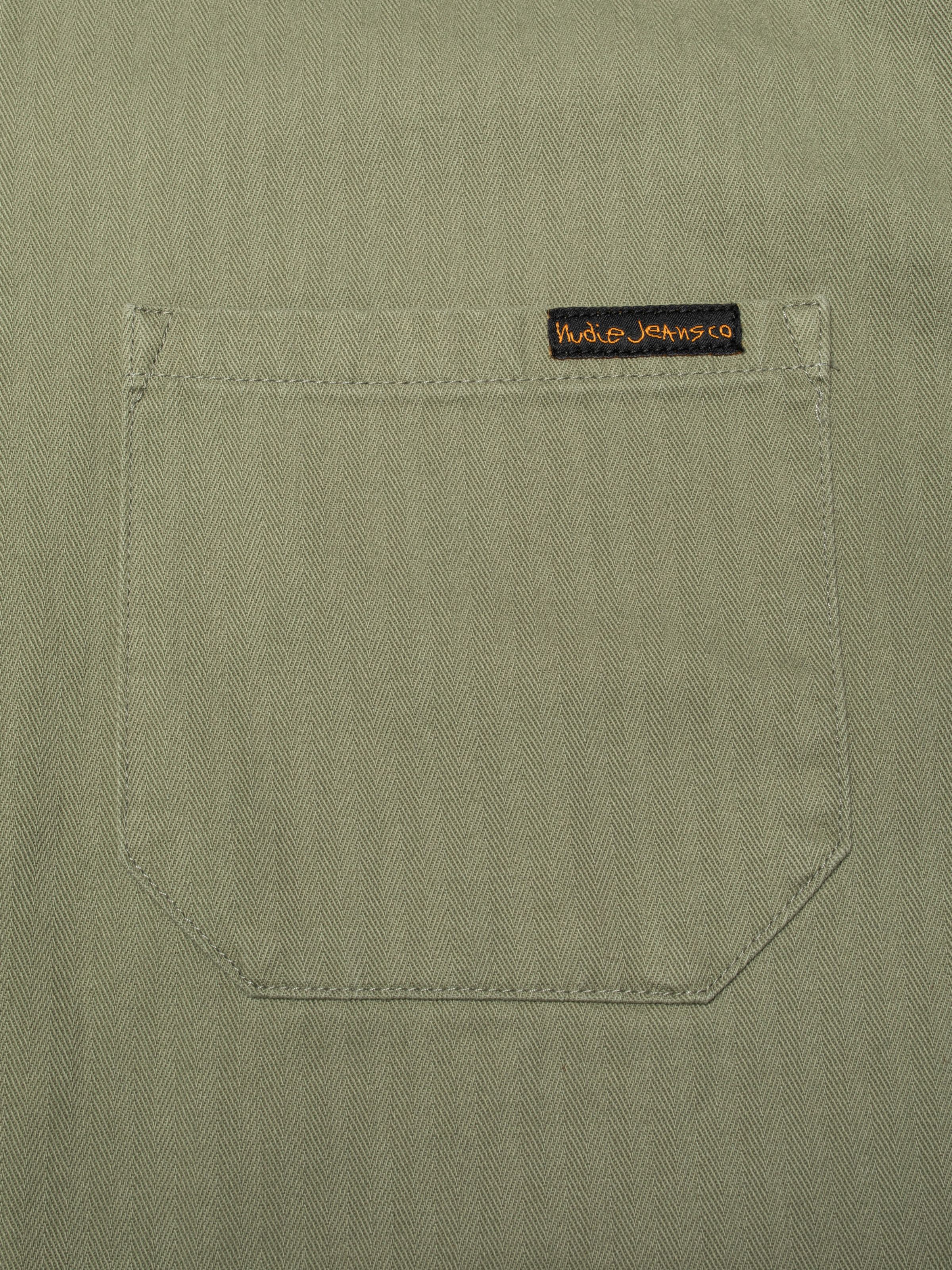 Nudie Jeans Buddy Chore Jacket Herringbone in Pale Green, close-up of the chest pocket and herringbone twill fabric.