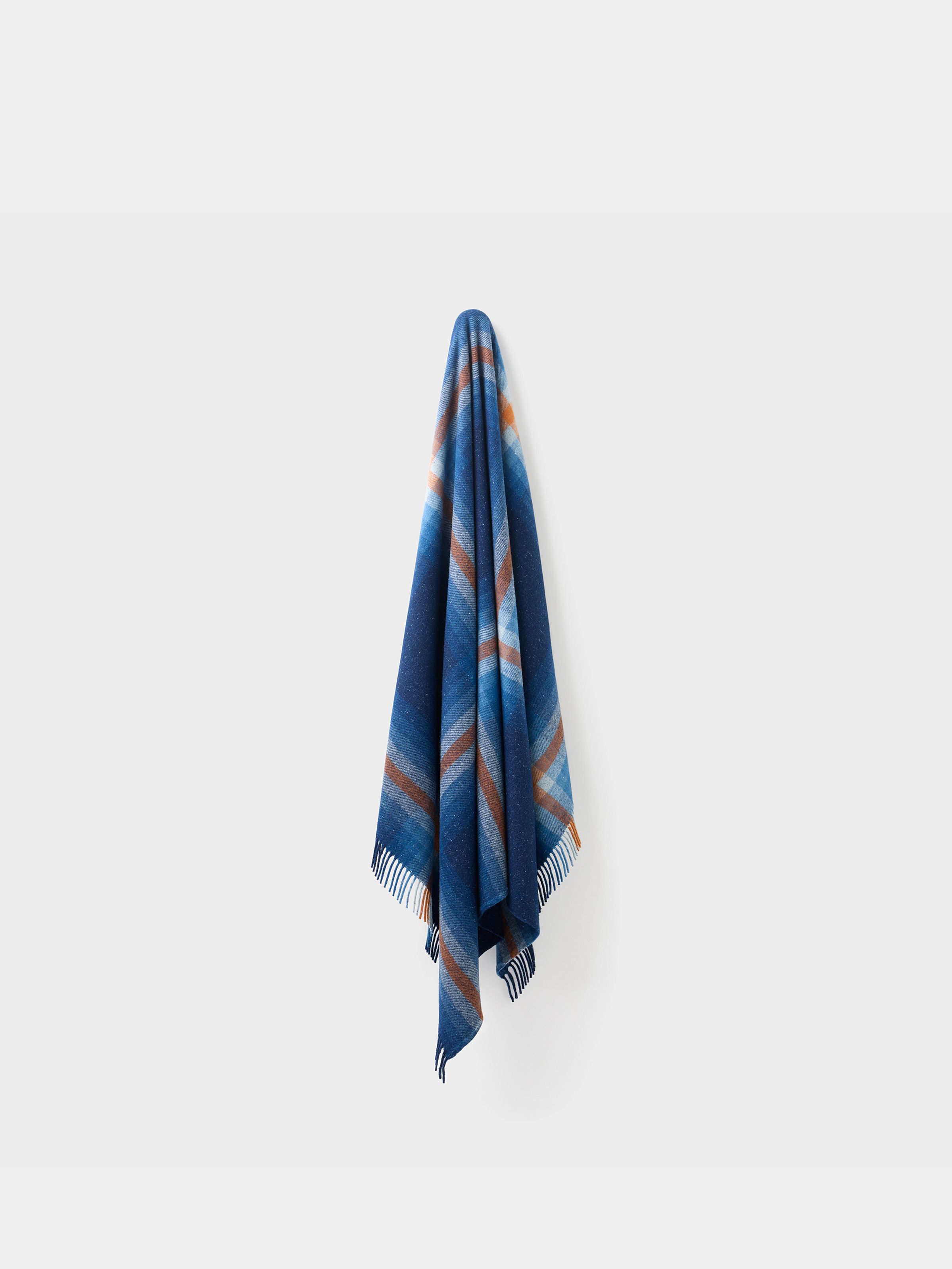 Nudie Jeans NJ x WM Recycled Blanket, a blue and brown striped recycled blanket, shown hanging against a plain wall.