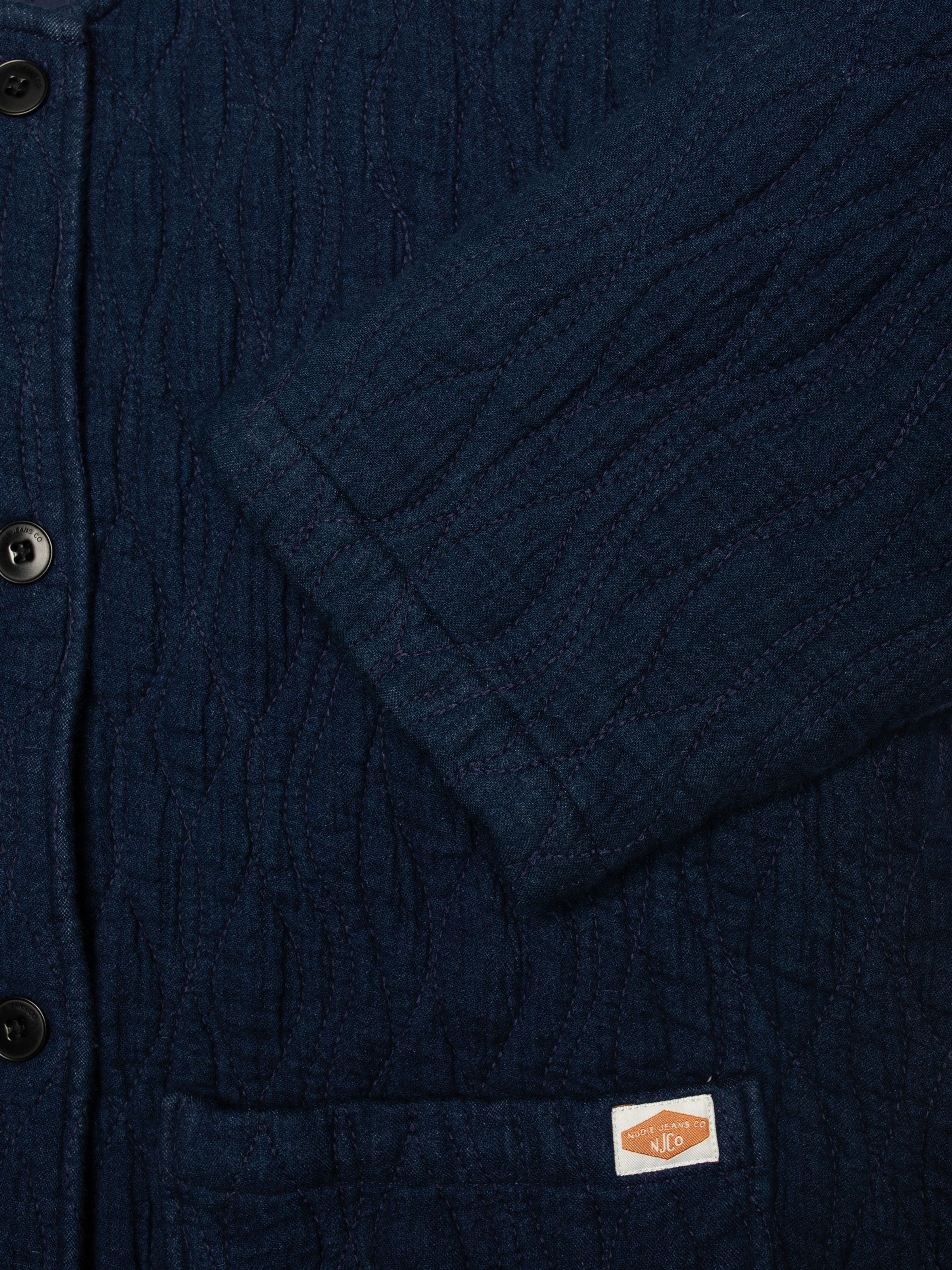 Nudie Jeans Sandra Jacket Indigo Quilt in blue, close-up showing the wavy quilted texture, sleeve, and front pocket detail.