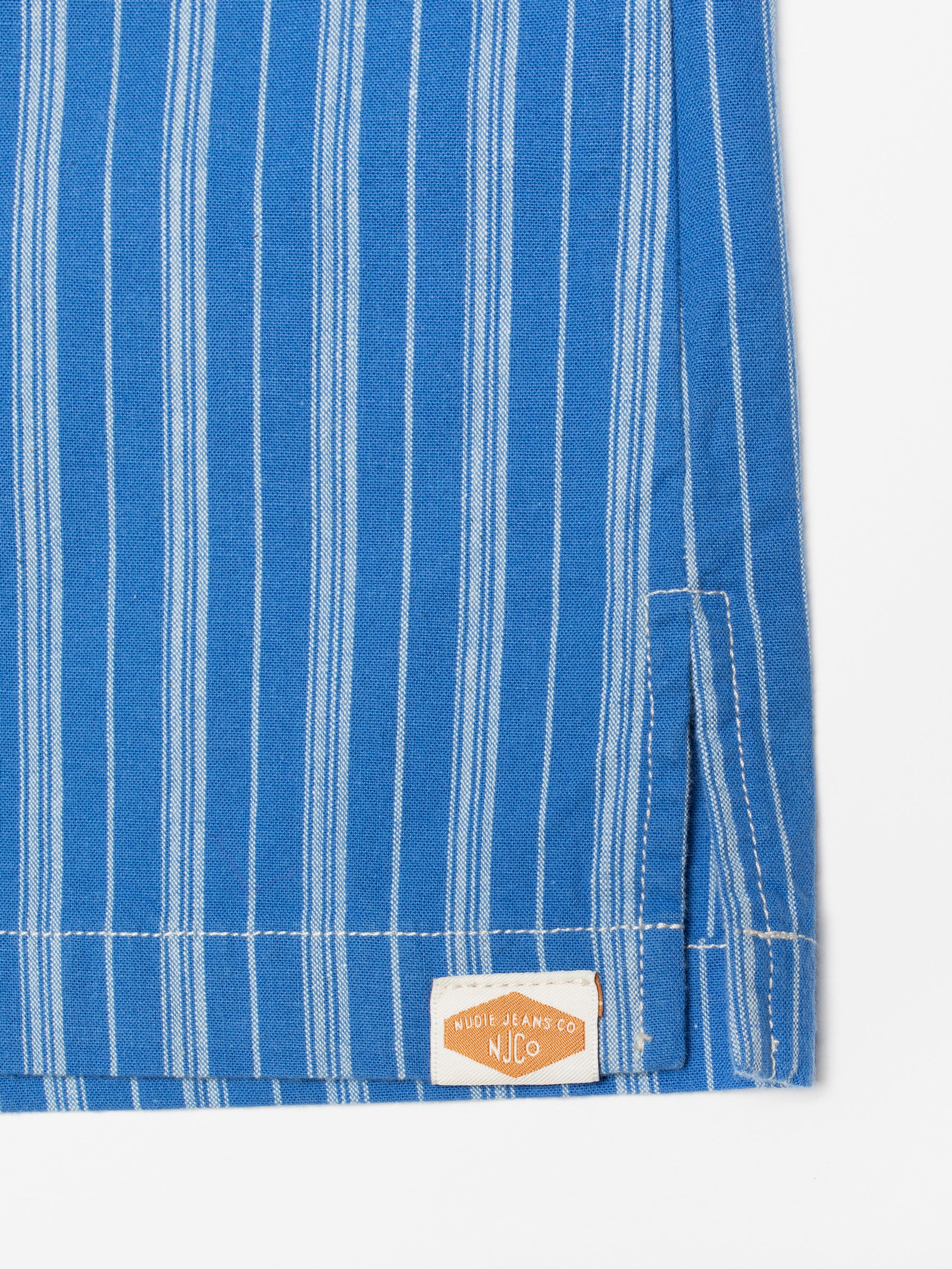 Nudie Jeans Jutta Shirt Striped, close-up of the side slit showing the woven logo label and off-white stitching.