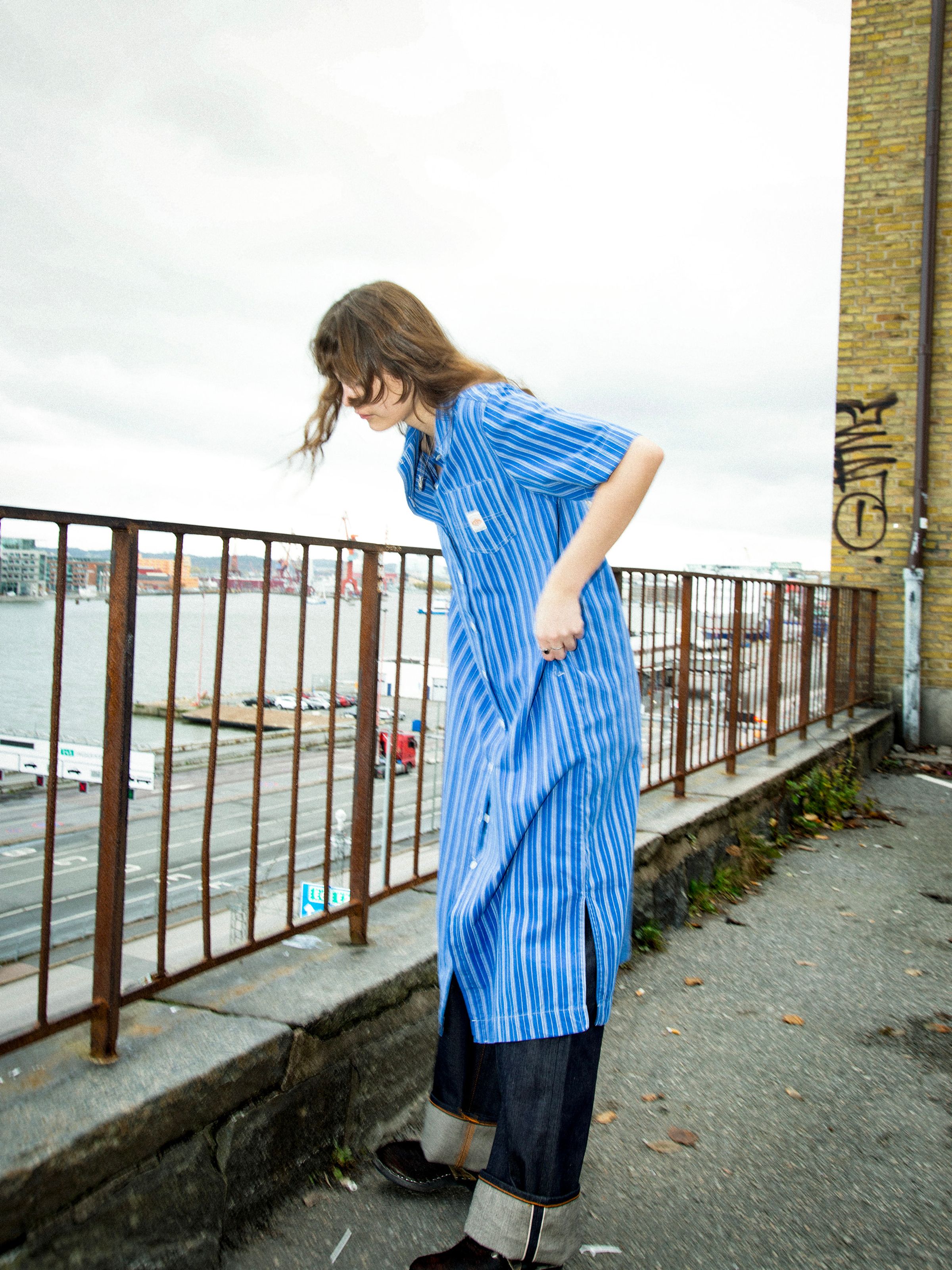 Nudie Jeans Danielle Dress Striped in Blue/Offwhite, women's shirt dress shown on a model styled over jeans outdoors.