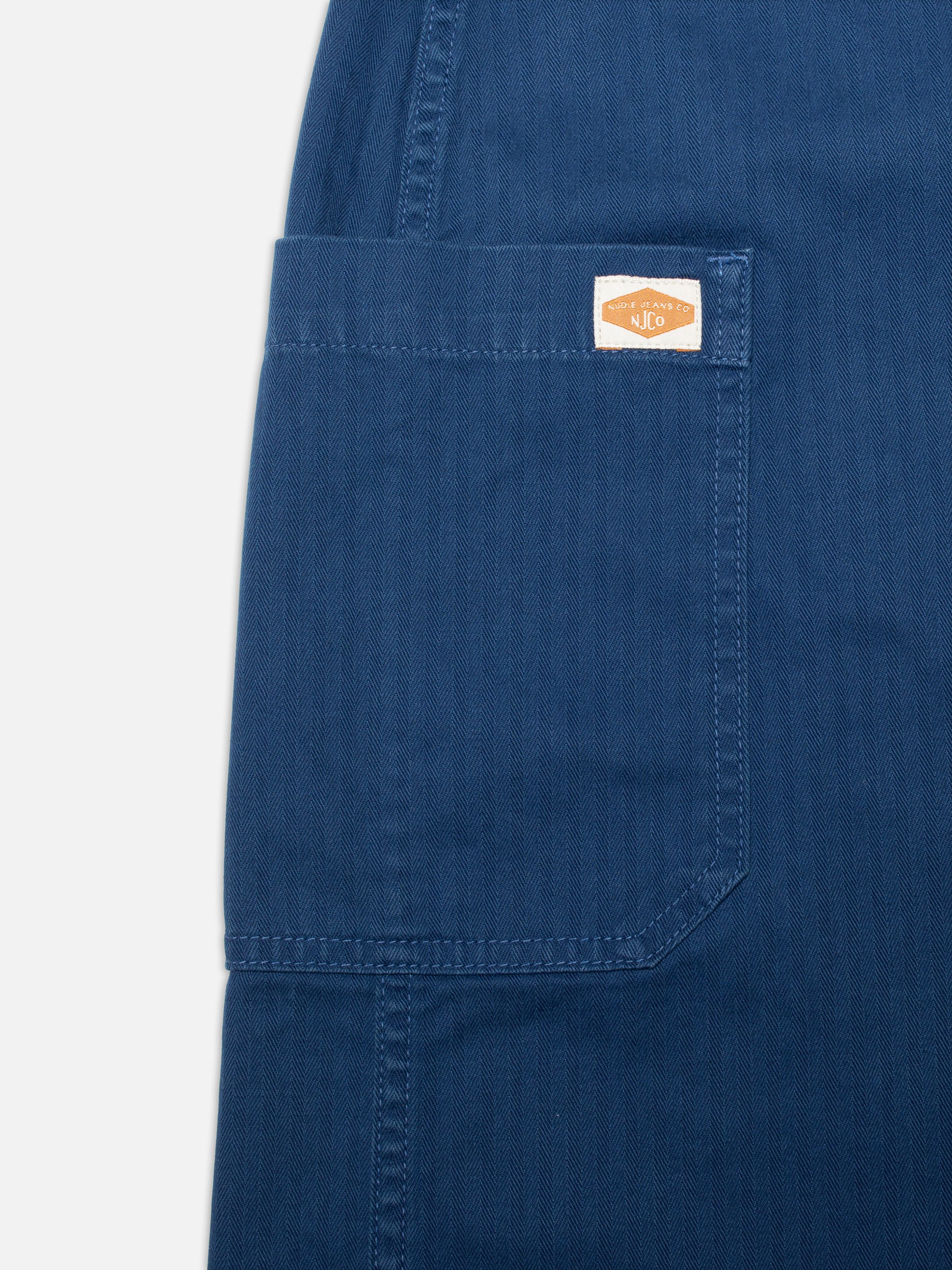 Nudie Jeans Irma Skirt Herringbone, a close-up of the blue herringbone fabric and the side pocket with the logo label.