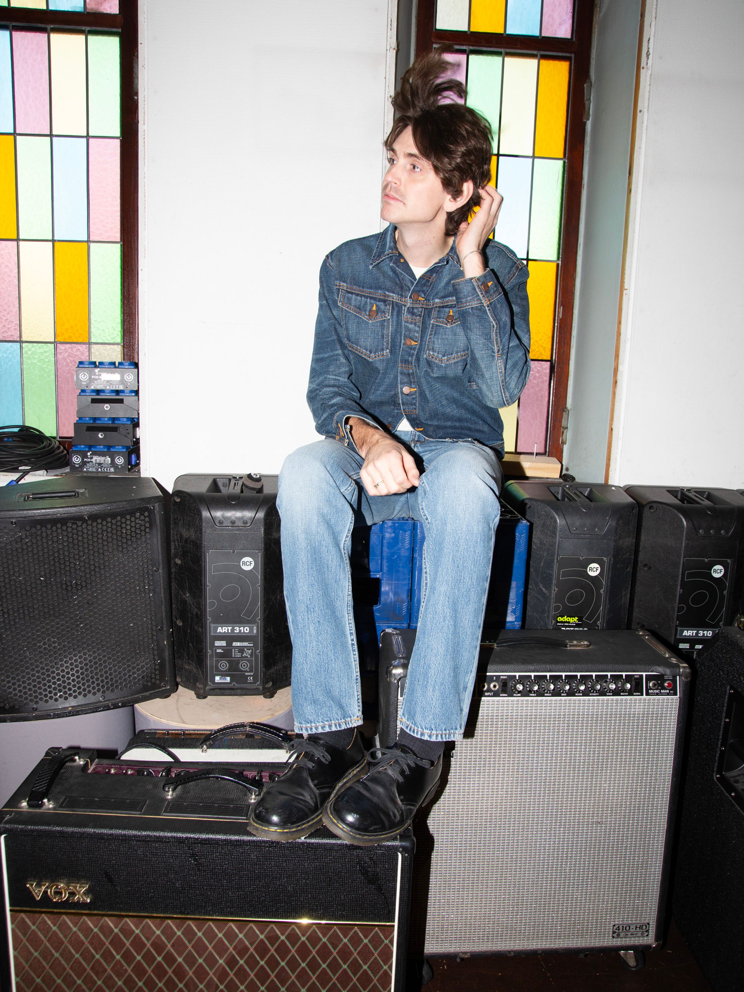 Nudie Jeans Gritty Jackson Cool Blue, men's regular fit straight leg jeans, shown on a model sitting on speakers.