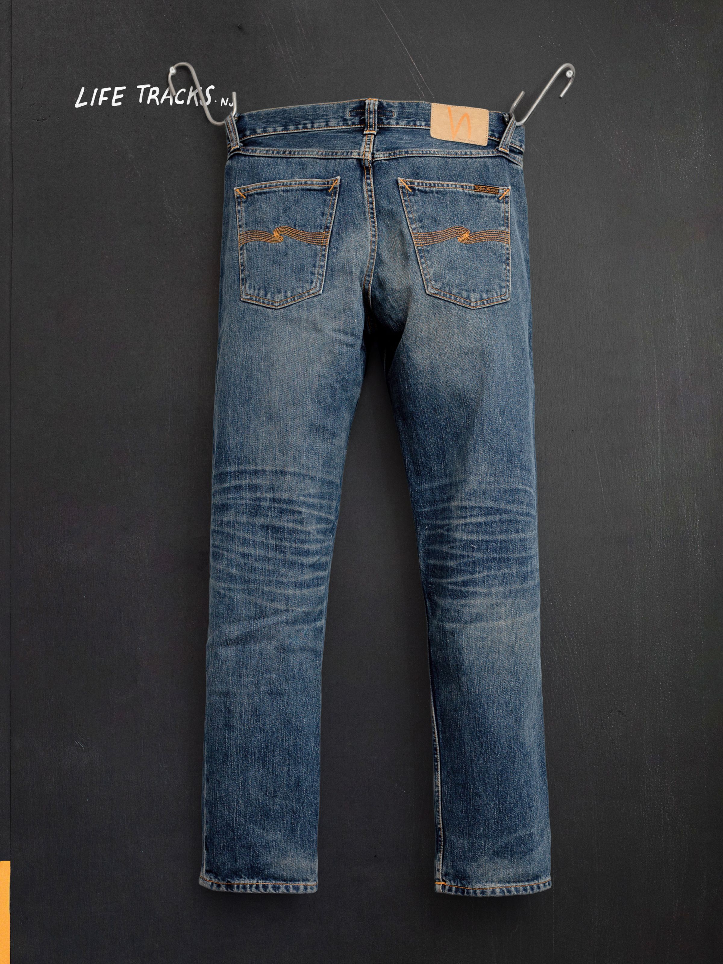 Nudie Jeans Gritty Jackson Sand Tracks, men's regular fit jeans, shown from the back hanging against a dark background.