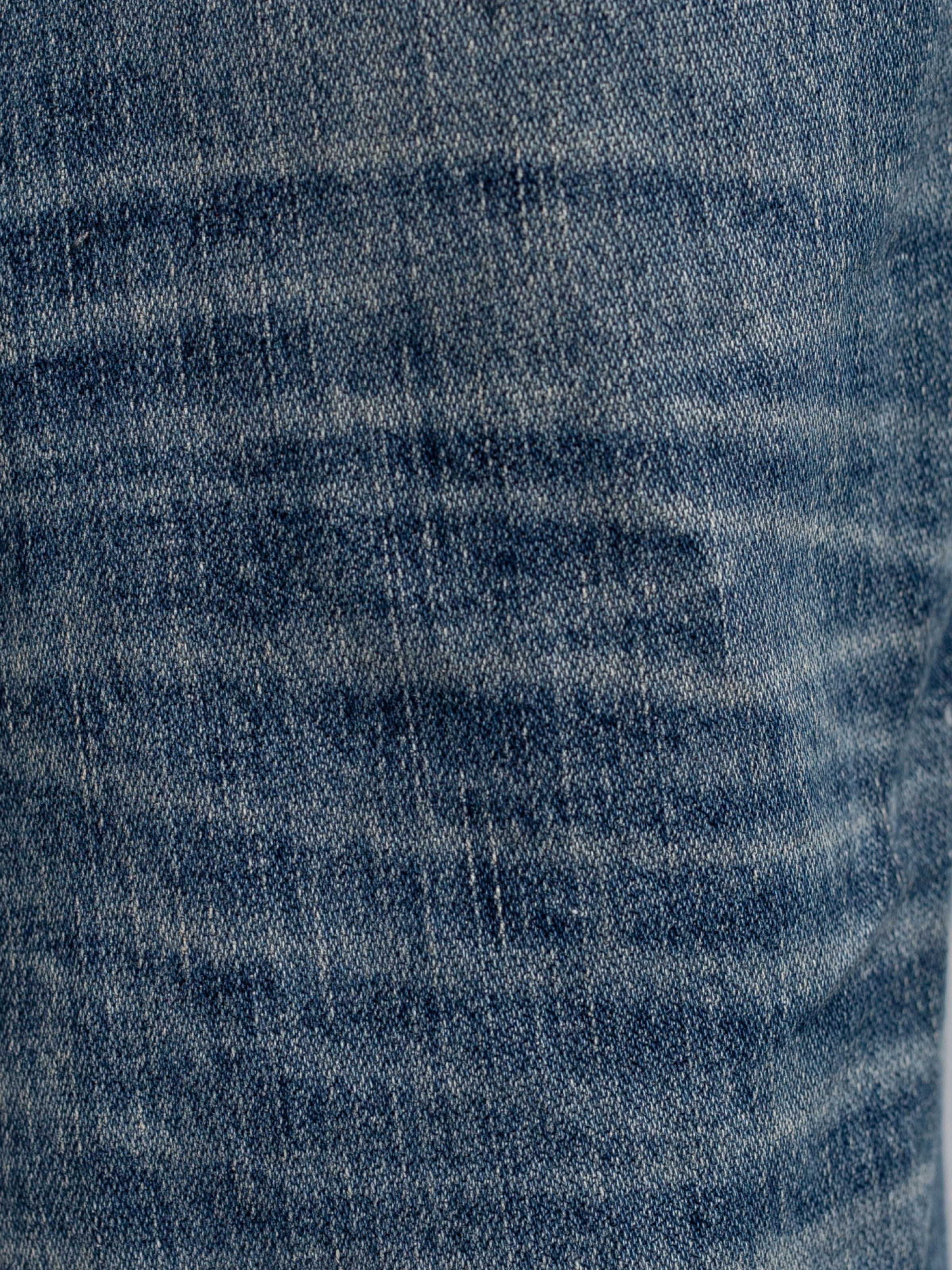 Nudie Jeans Gritty Jackson Sand Tracks, men's regular fit jeans, close-up of the mid-blue wash denim fabric texture.