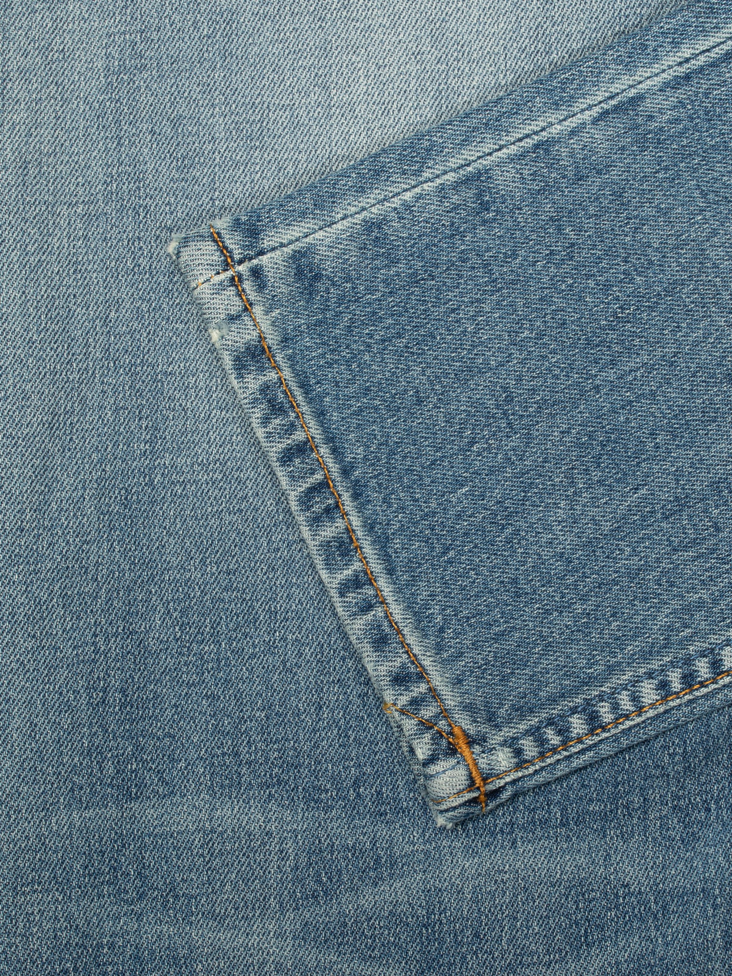 Nudie Jeans Solid Ollie Salt Water, men's slim fit jeans, close-up of a back pocket's tobacco stitching and texture.
