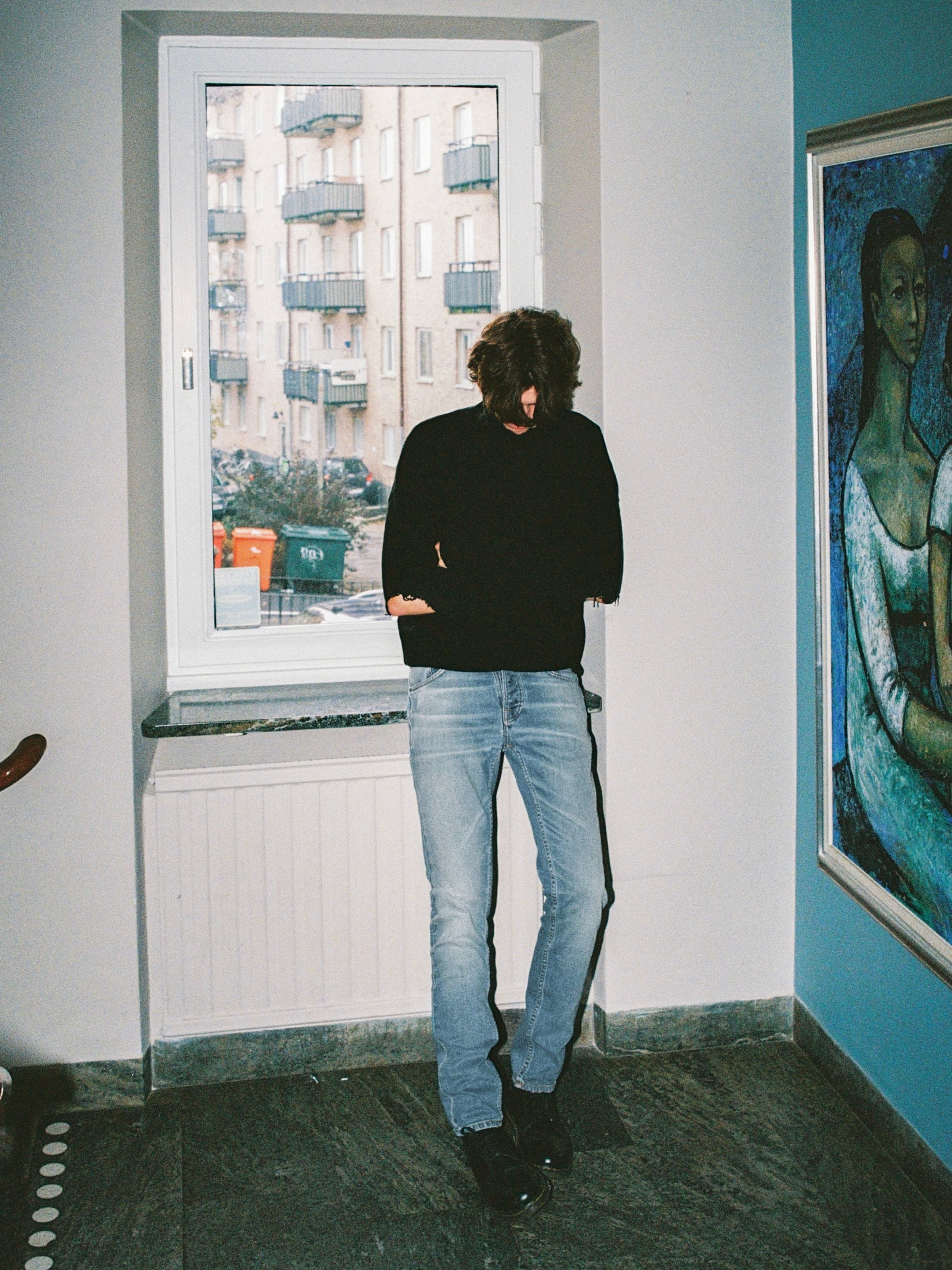 Nudie Jeans Solid Ollie Salt Water, men's slim fit straight leg jeans shown full length on a model standing by a window.