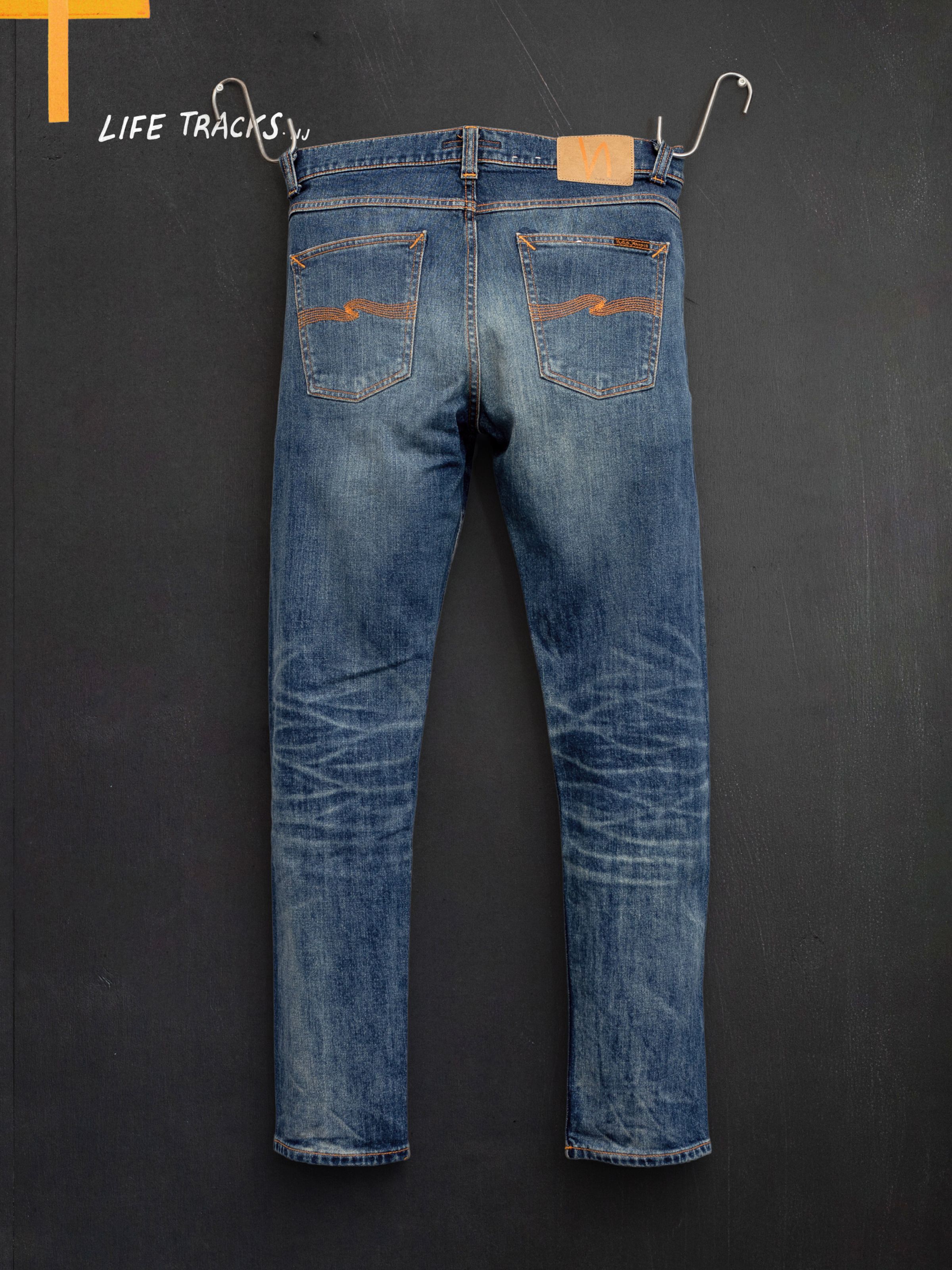 Nudie Jeans Lean Dean Salty Tracks, men's slim tapered jeans hanging against a wall, showing the back.