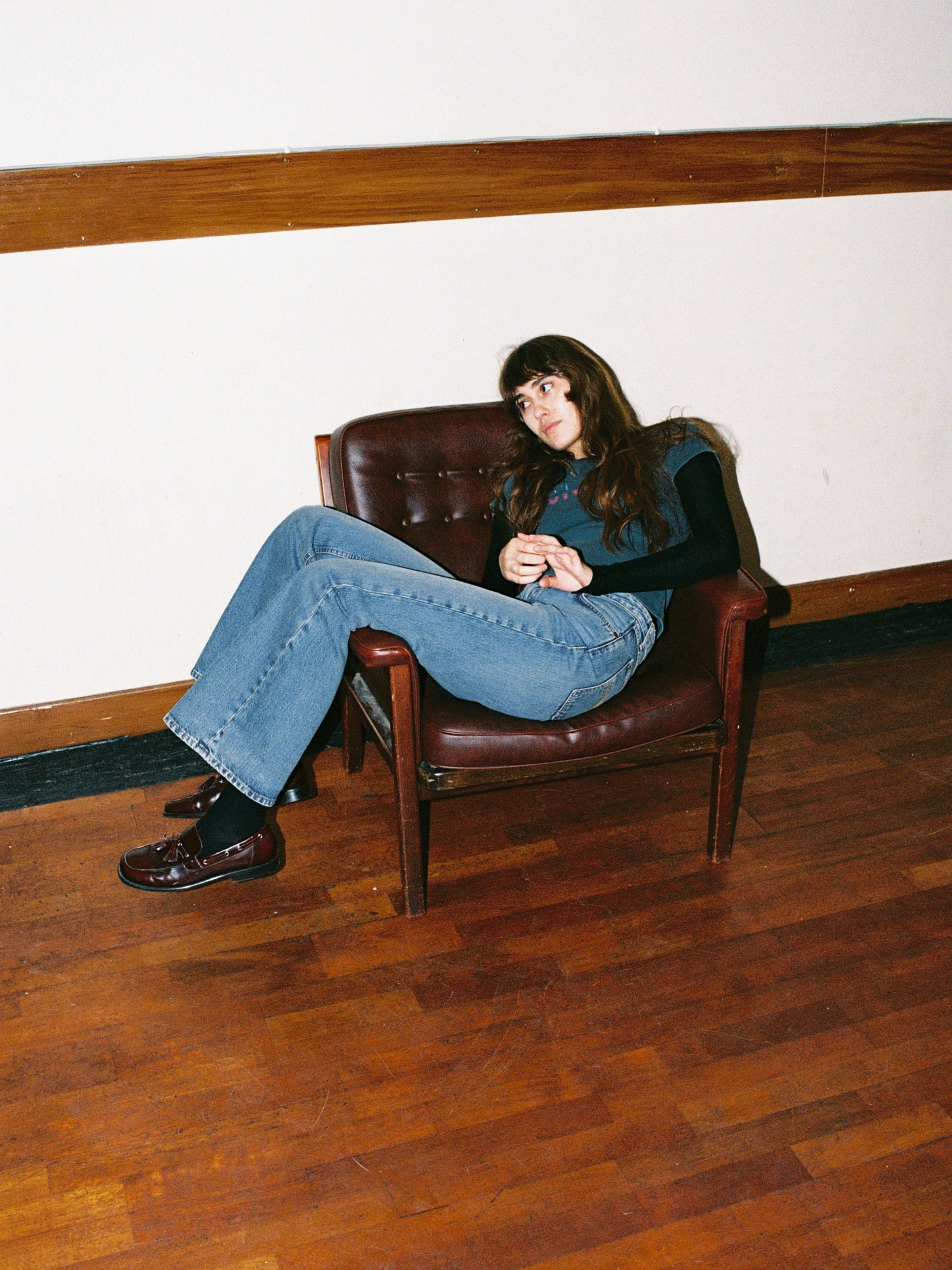 Nudie Jeans Dusty Dee Streaky Wash, Damenjeans mit ausgestelltem Bein, an einem Model, das in einem Ledersessel sitzt.