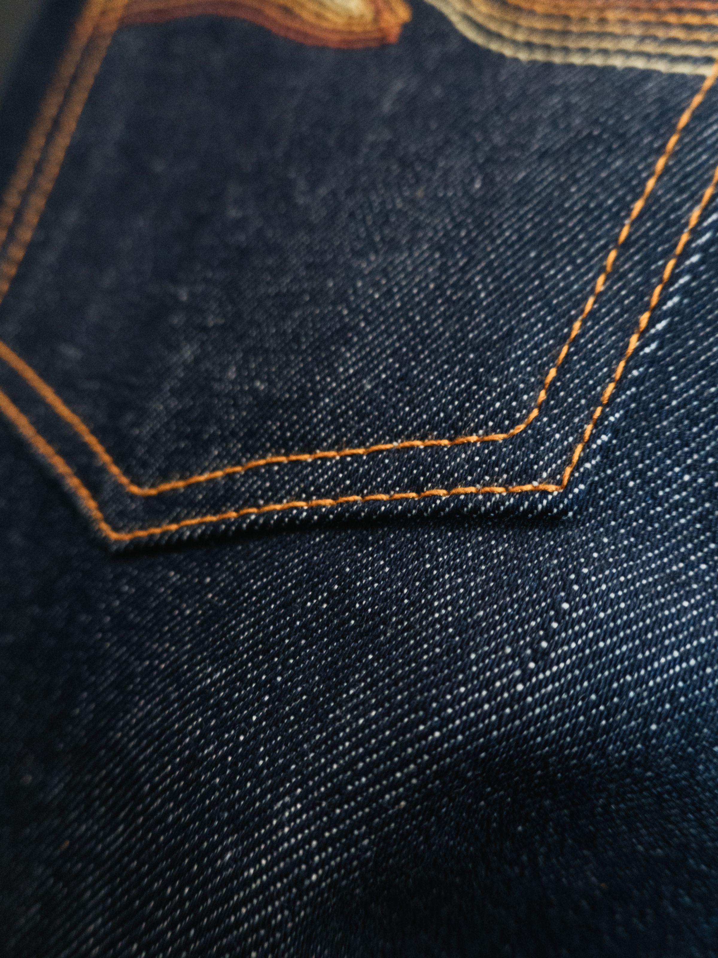 Nudie Jeans Solid Ollie Dry Sunburns, a men's slim fit jean, shown in a close-up of the back pocket gradient embroidery.