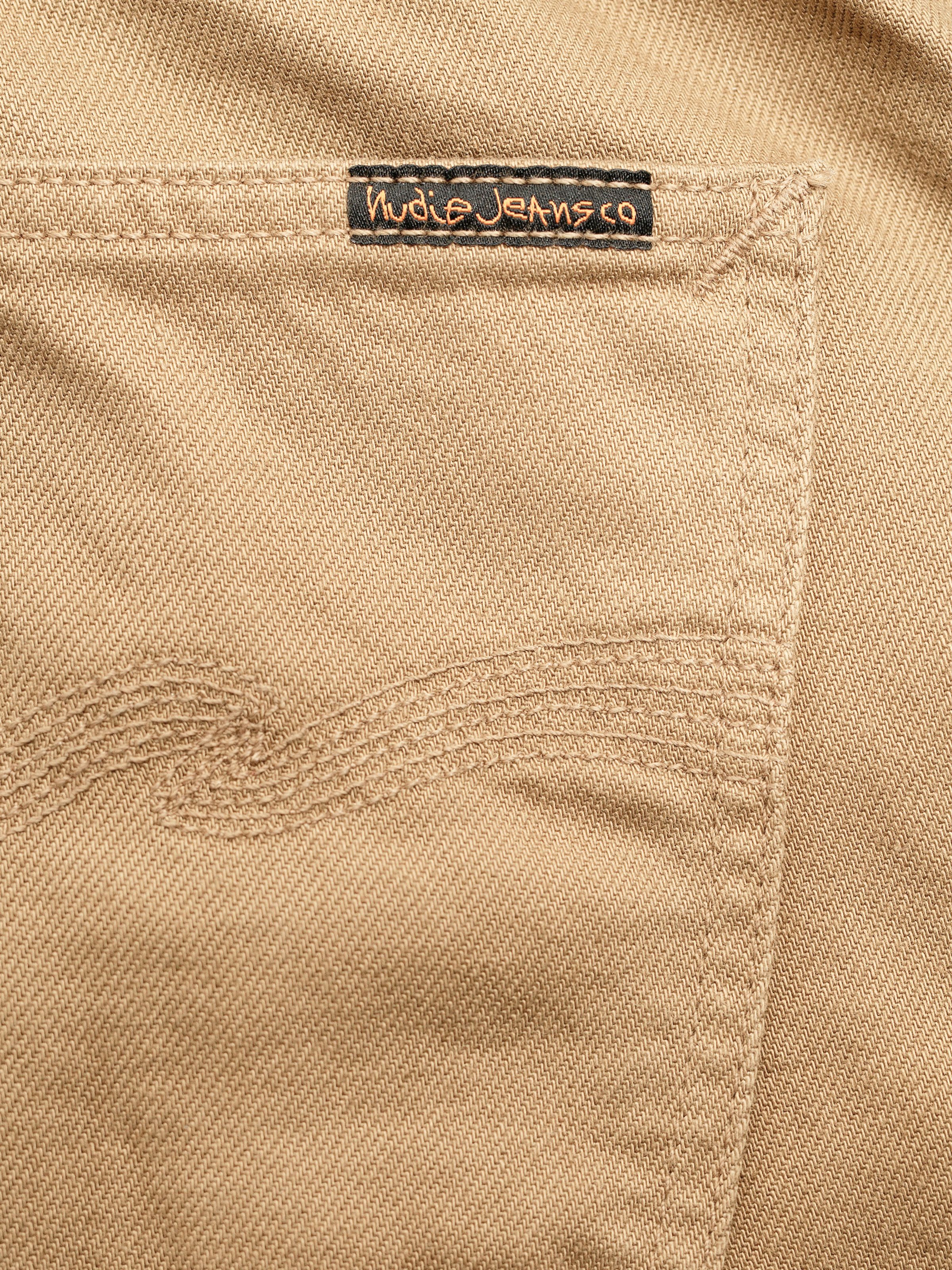 Nudie Jeans Gritty Jackson Everlion, close-up of the back pocket showing the black logo patch and signature embroidery.
