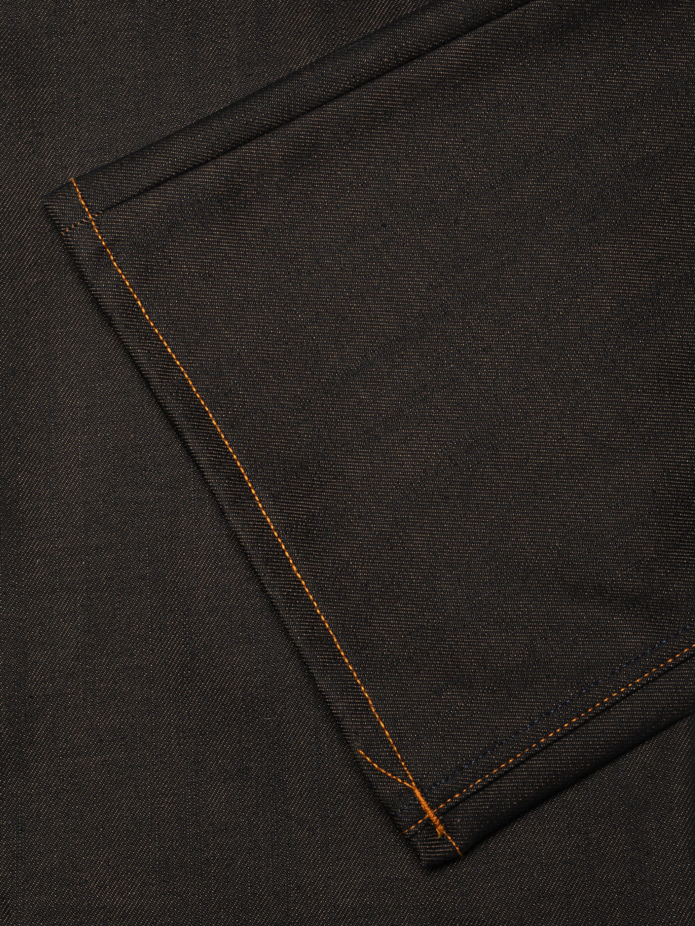 Nudie Jeans Flare Glenn in Dry Blue, Nahaufnahme des Saums, die den dunklen Rigid Denim und die orangen Nähte zeigt.