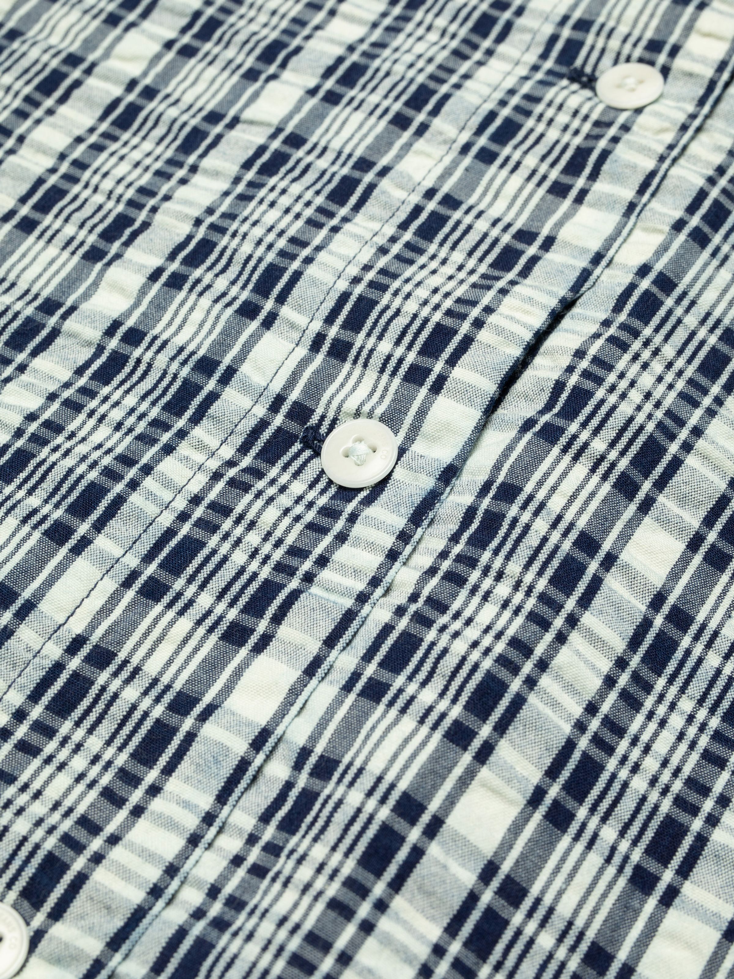 Nudie Jeans Jutta Shirt Indigo Seersucker, close-up of the indigo and off-white checked fabric and a white button.