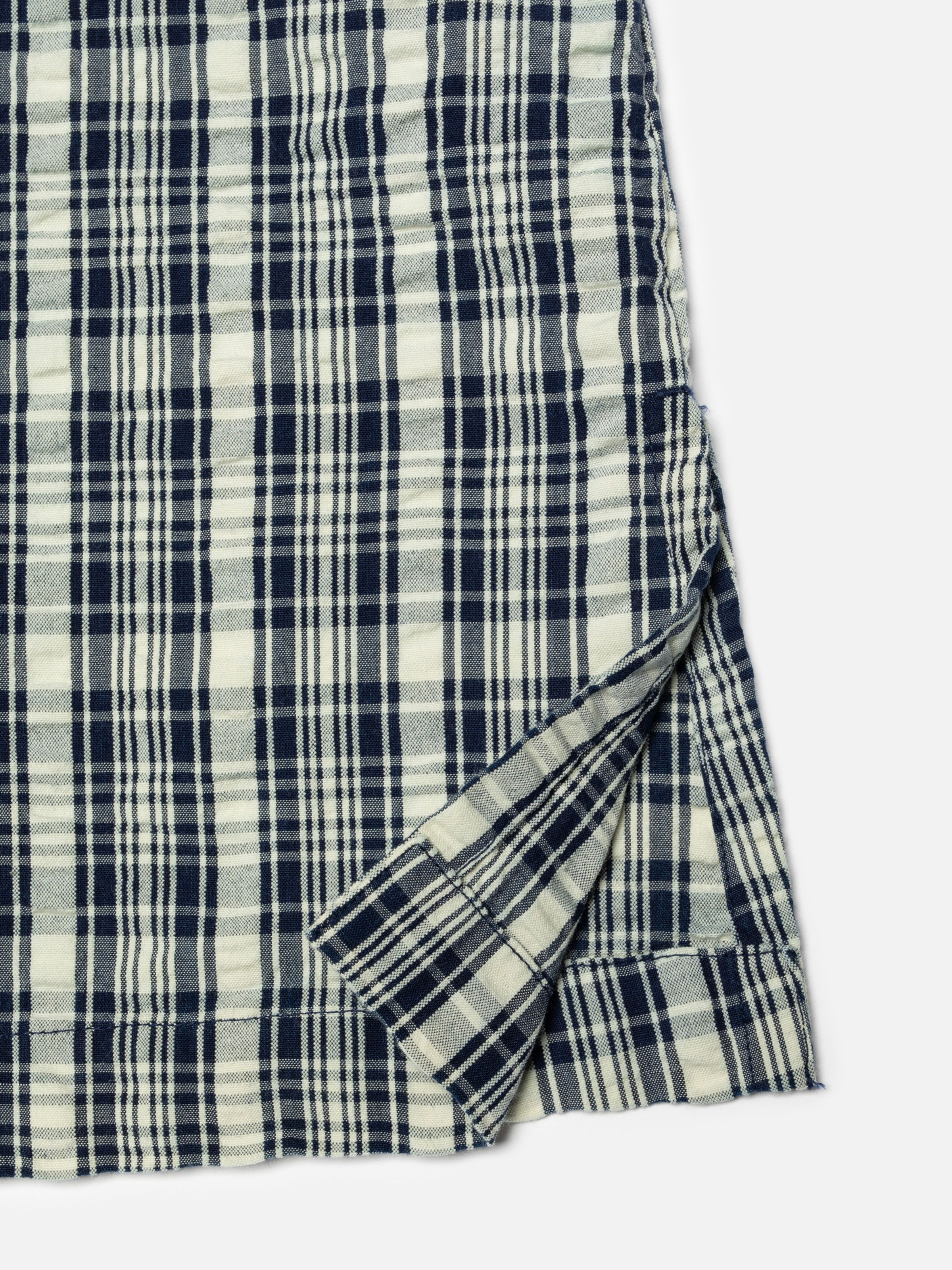 Nudie Jeans Ronja Dress Indigo Seersucker, close-up of the hem and side slit showing the indigo yarn check pattern.