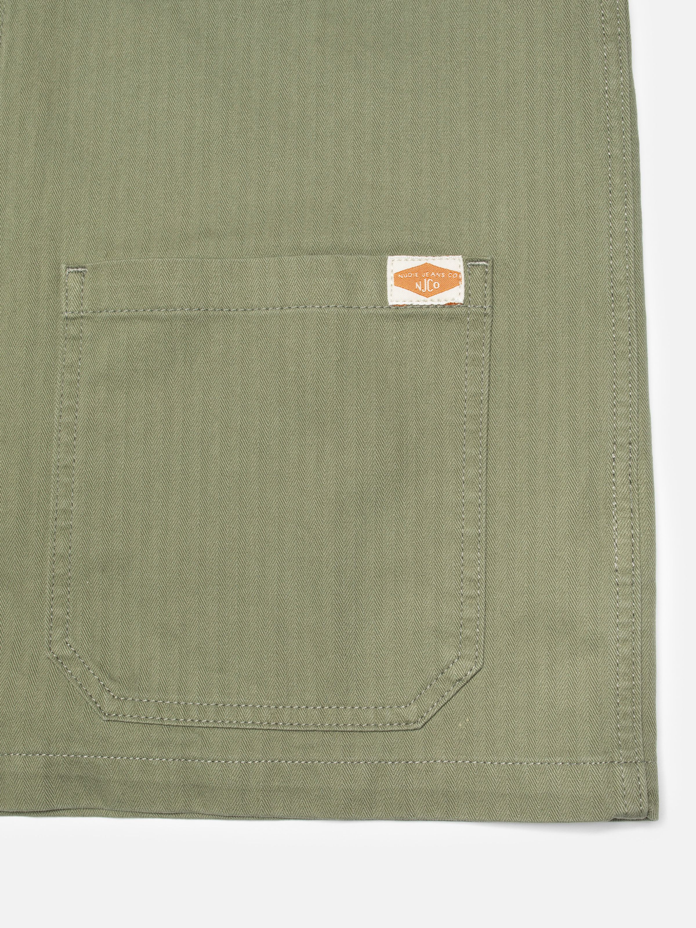 Nudie Jeans Lovis Herringbone Jacket in Pale Green, a close-up of the front patch pocket showing the fabric texture.