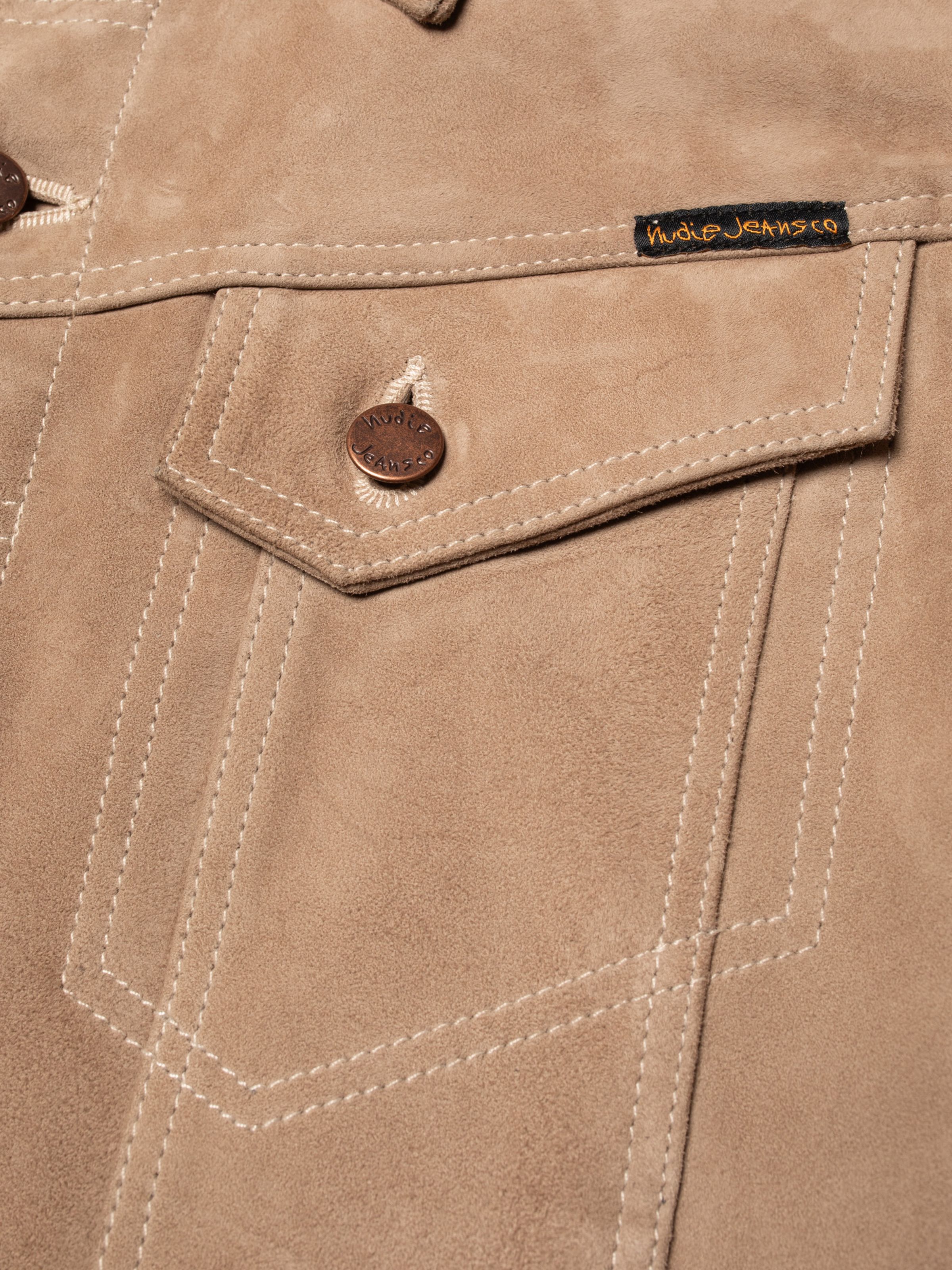 Nudie Jeans Willy Suede Jacket in Mud, close-up of the chest pocket showing the copper logo button and logo label.