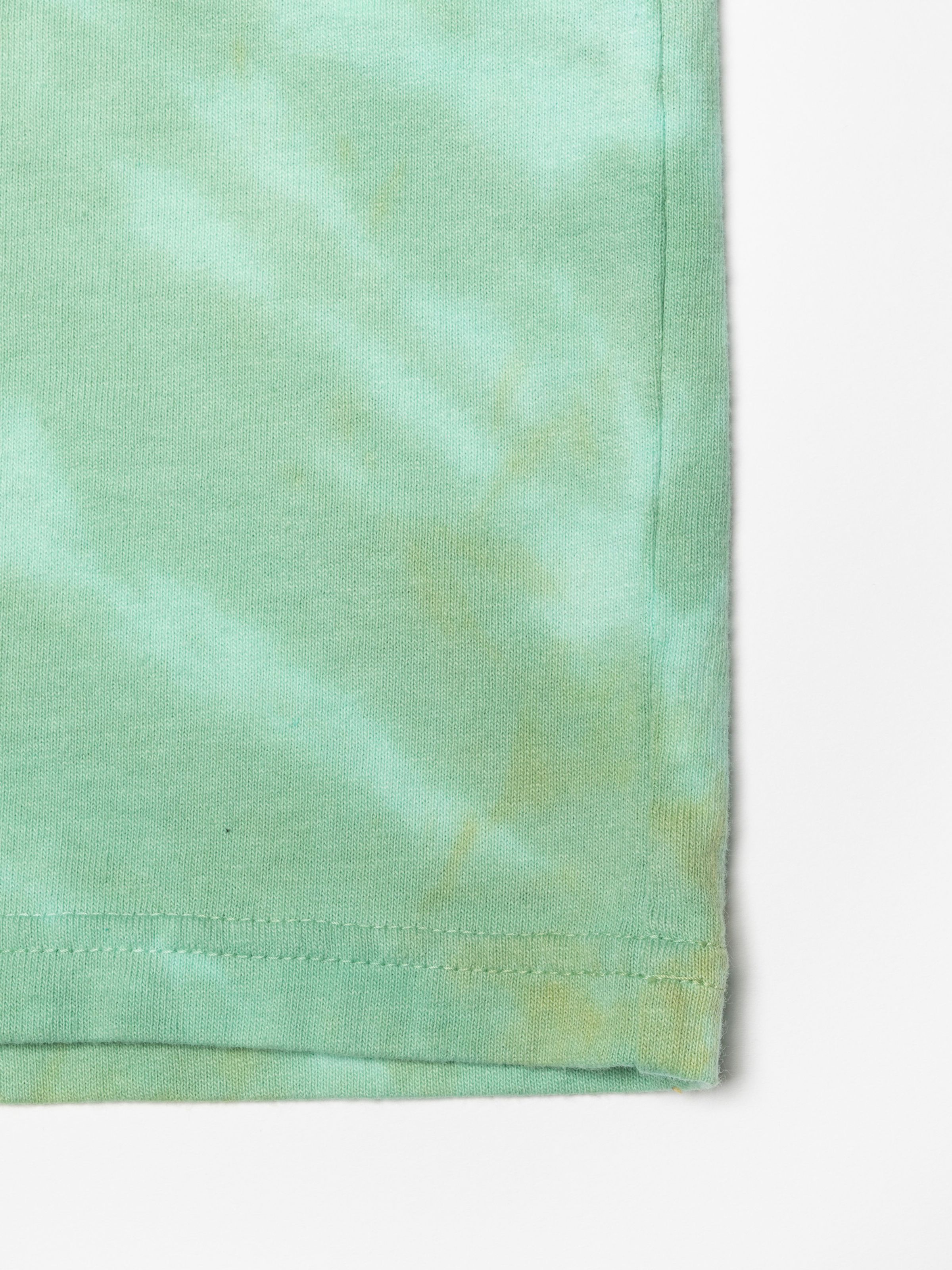 Nudie Jeans Koffe T-Shirt Chameleon Turquoise, close-up of the tie-dye organic cotton jersey fabric and hem.
