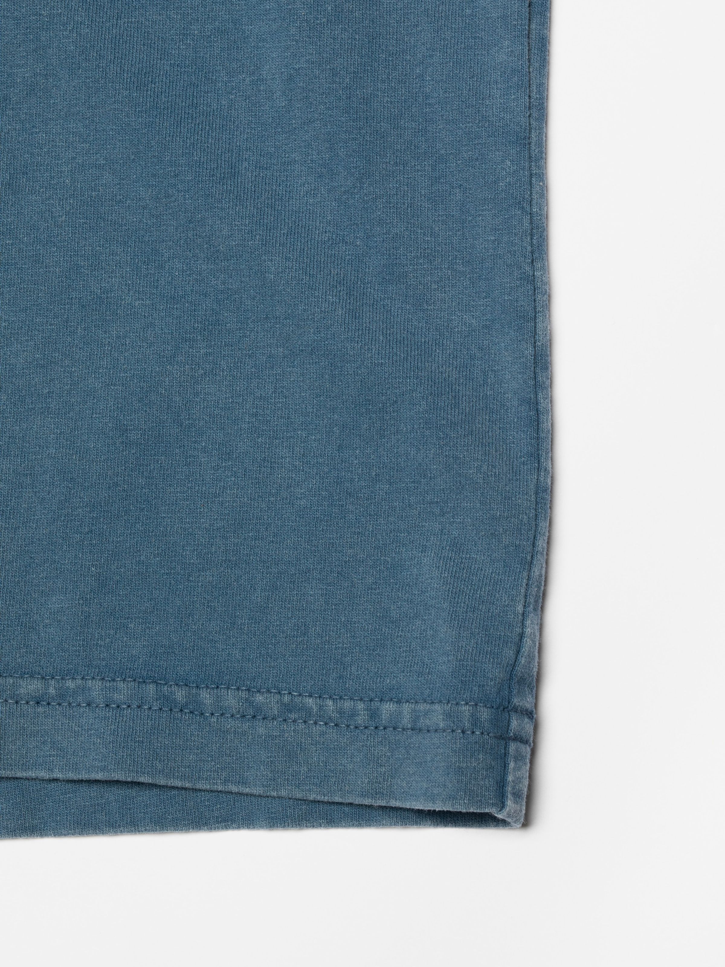 Nudie Jeans Roy T-Shirt OG Line-Up in French Blue, close-up of the hem and garment-dyed organic cotton fabric.