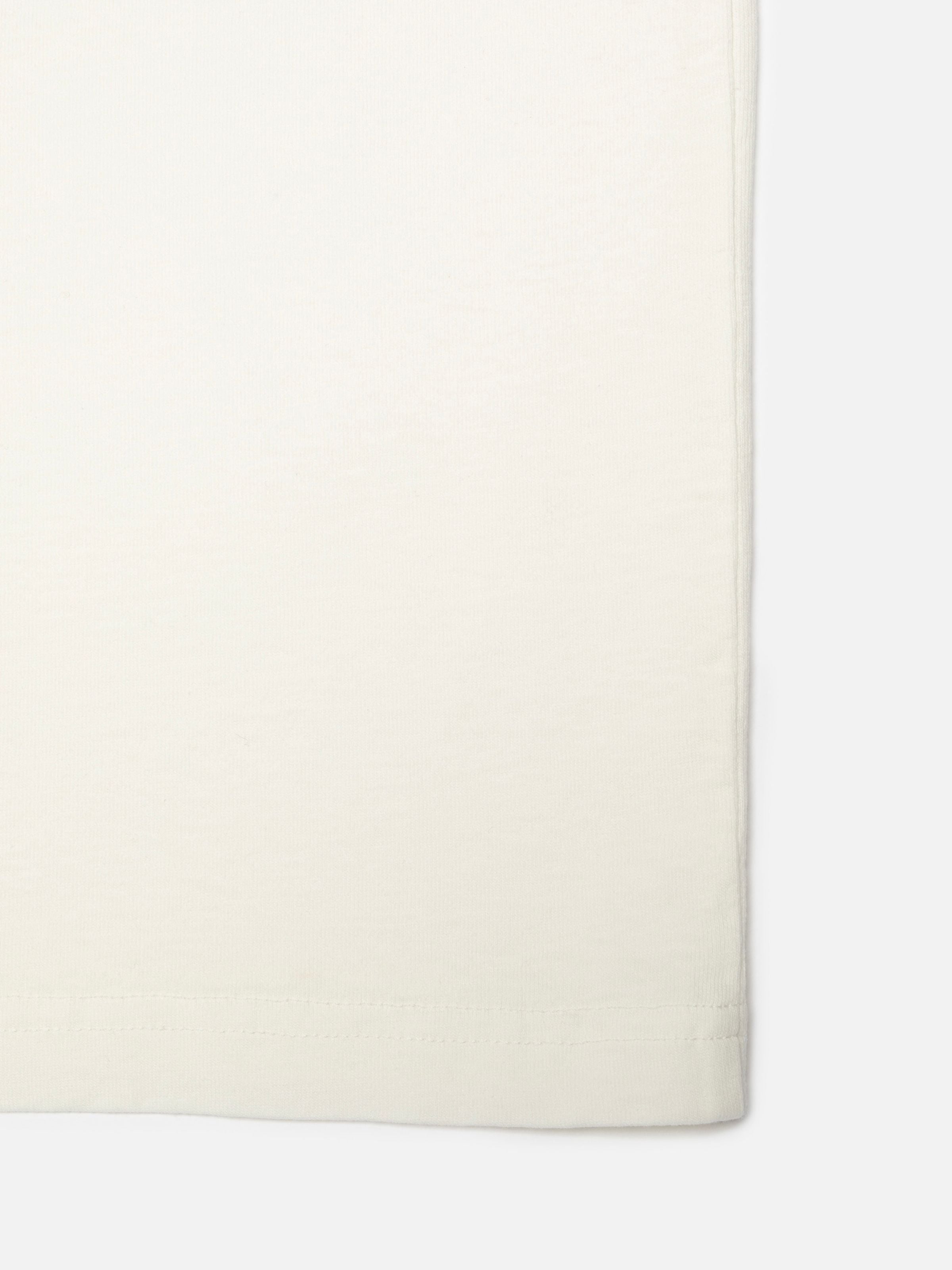 Nudie Jeans Roy T-Shirt NJCO Pin in Chalk White, close-up of the organic cotton fabric and bottom hem stitching.