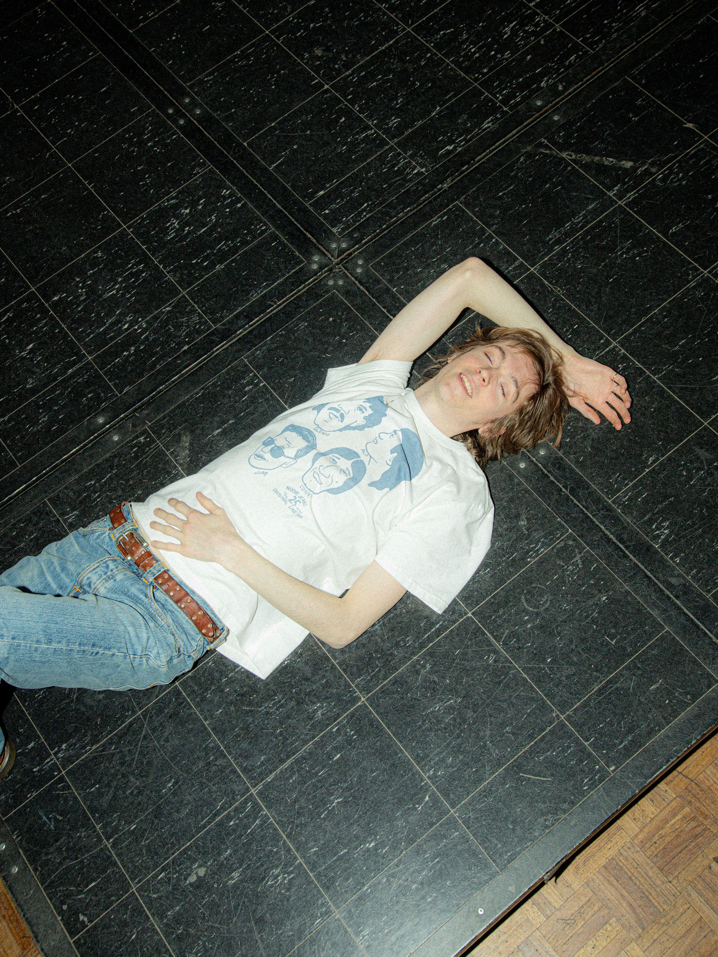 Nudie Jeans Roy T-Shirt Fab Four in Chalk White, organic cotton tee with a graphic print, shown on a model lying down.