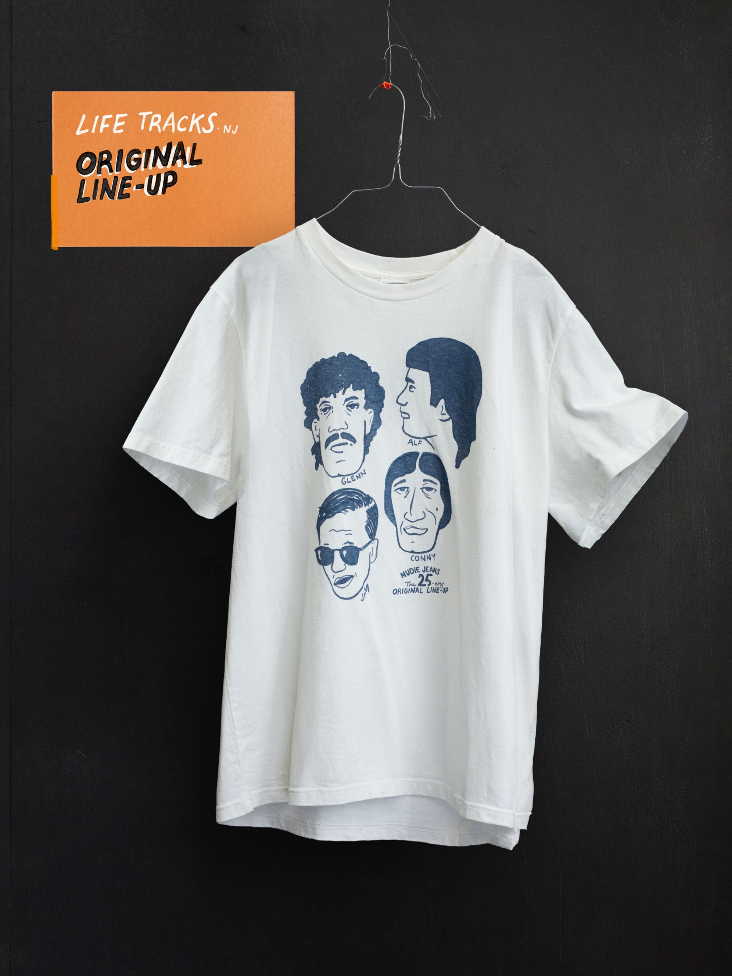 Nudie Jeans Roy T-Shirt Fab Four in Chalk White, an organic cotton relaxed-fit tee with a graphic print on a hanger.