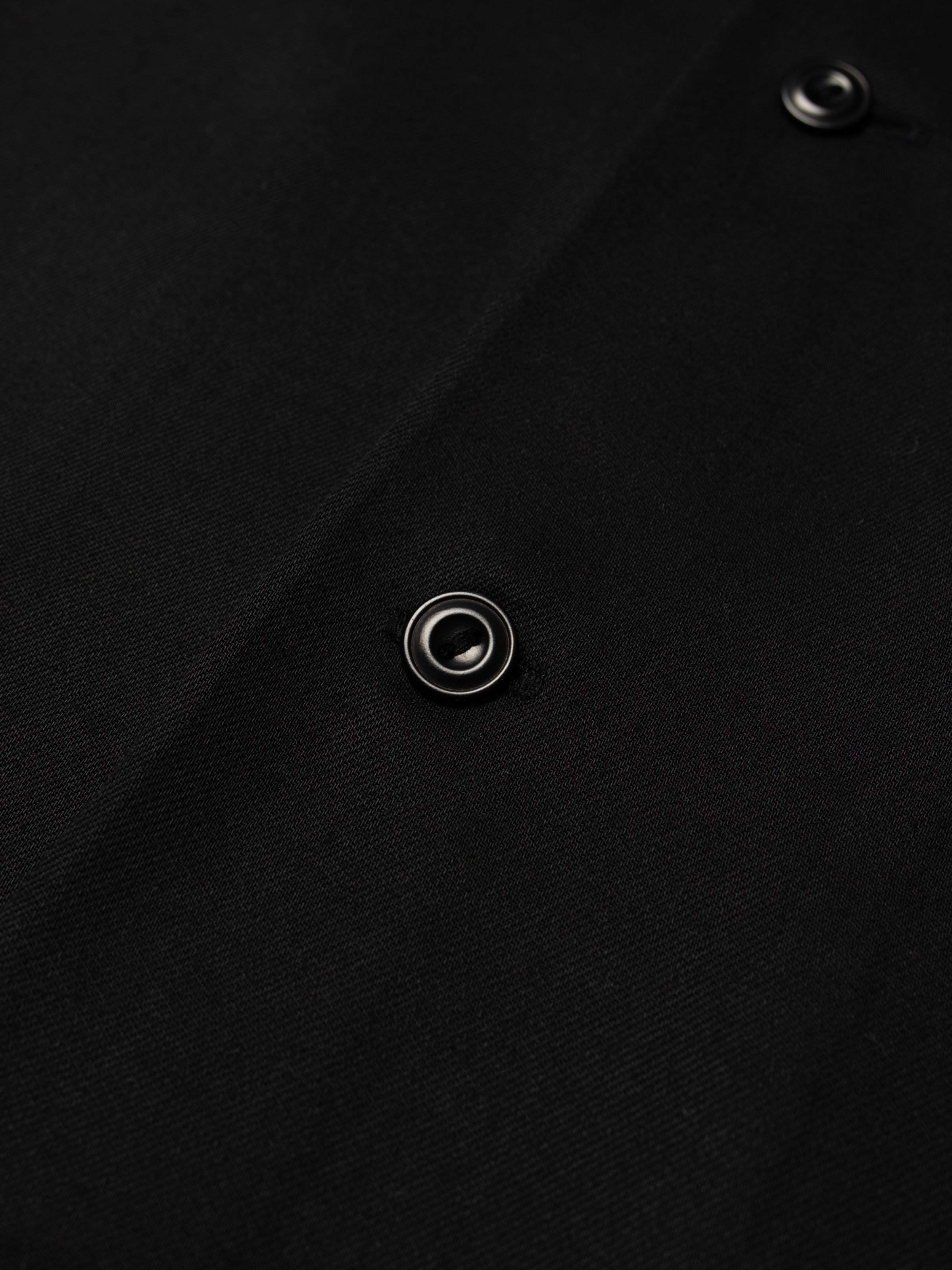 Nudie Jeans Arthur Bowling Shirt Saftey Pin, close-up of a corozo button on black TENCEL™ Lyocell fabric.