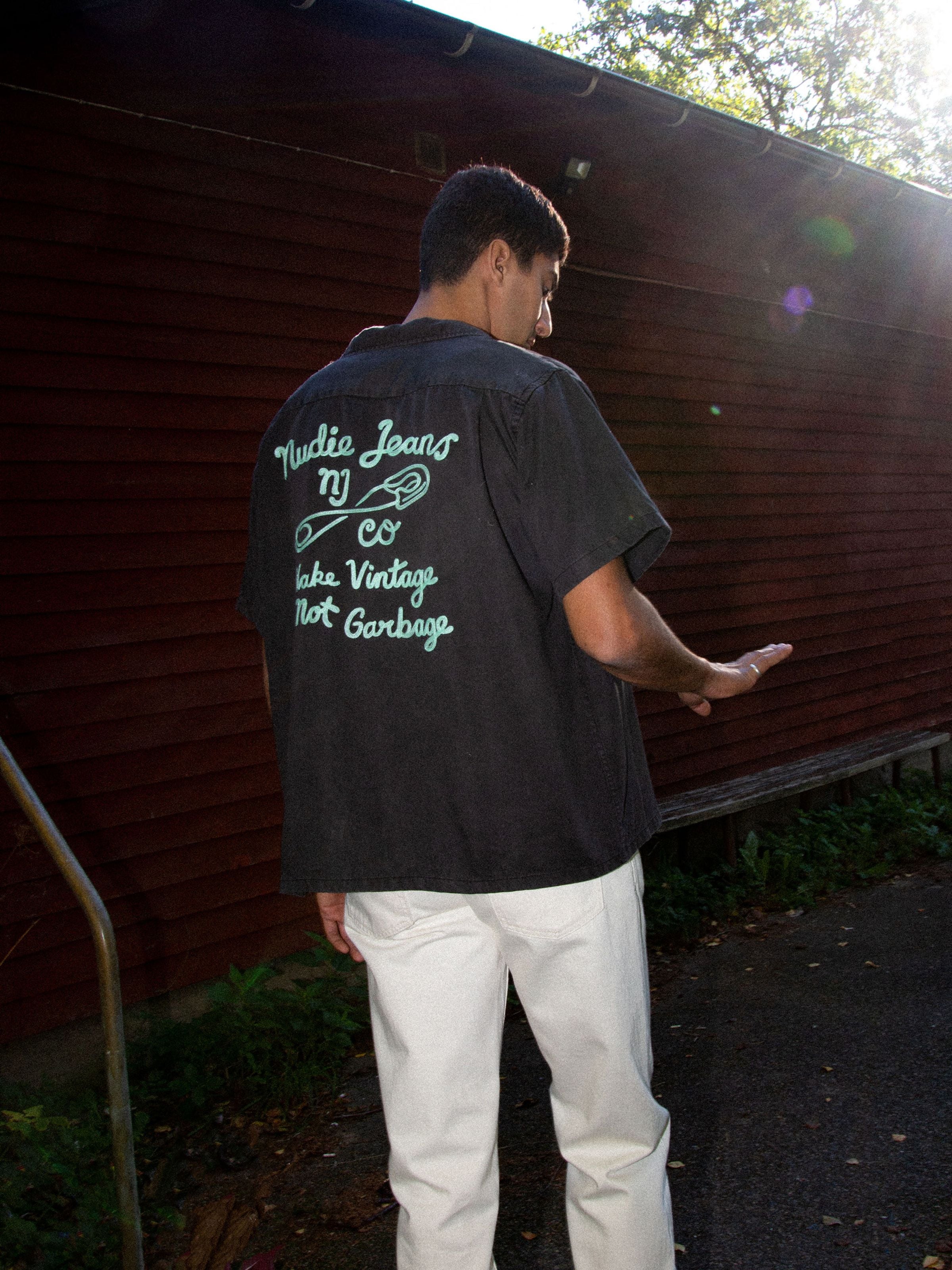 Nudie Jeans Arthur Bowling Shirt Saftey Pin, schwarzes Tencel-Hemd mit minzgrüner Rückenstickerei, an einem Model gezeigt.