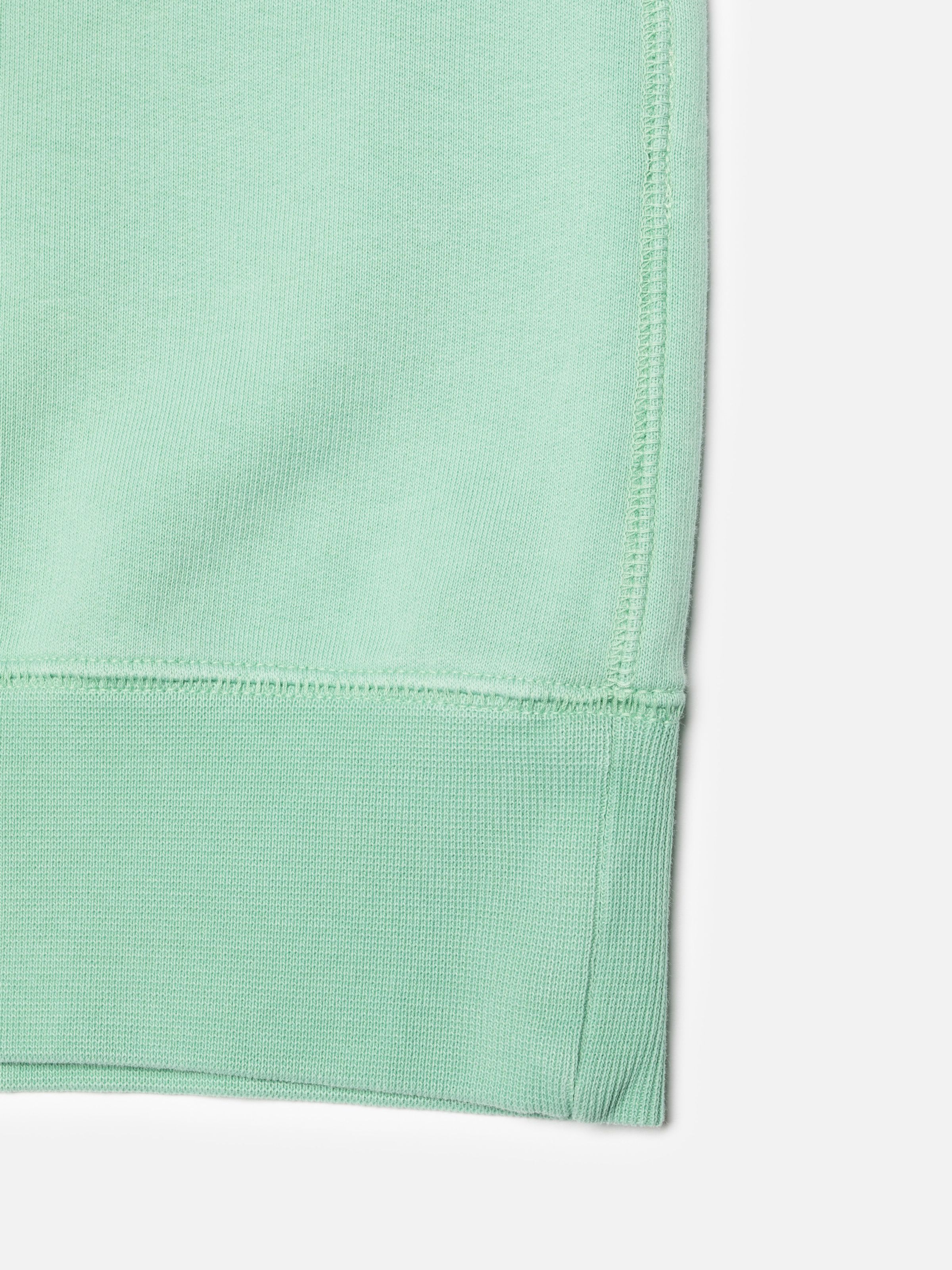 Nudie Jeans Palle Sweatshirt Take It Easy in Turquoise, close-up of the ribbed hem and flatlock stitching.