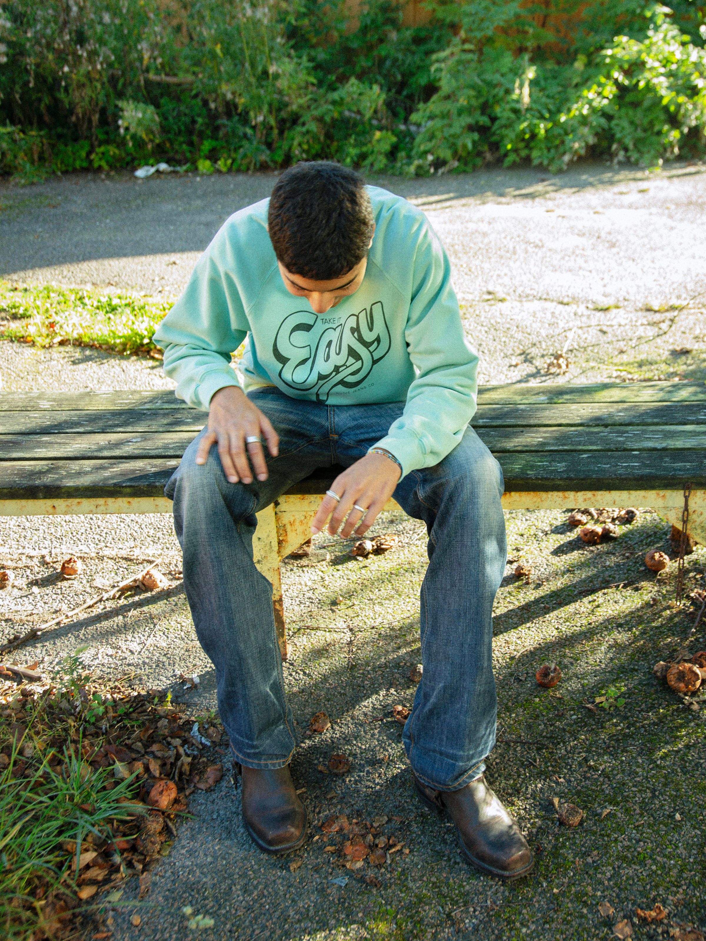 Nudie Jeans Palle Sweatshirt Take It Easy in turquoise, men's regular-fit sweatshirt with chest print shown on a model.