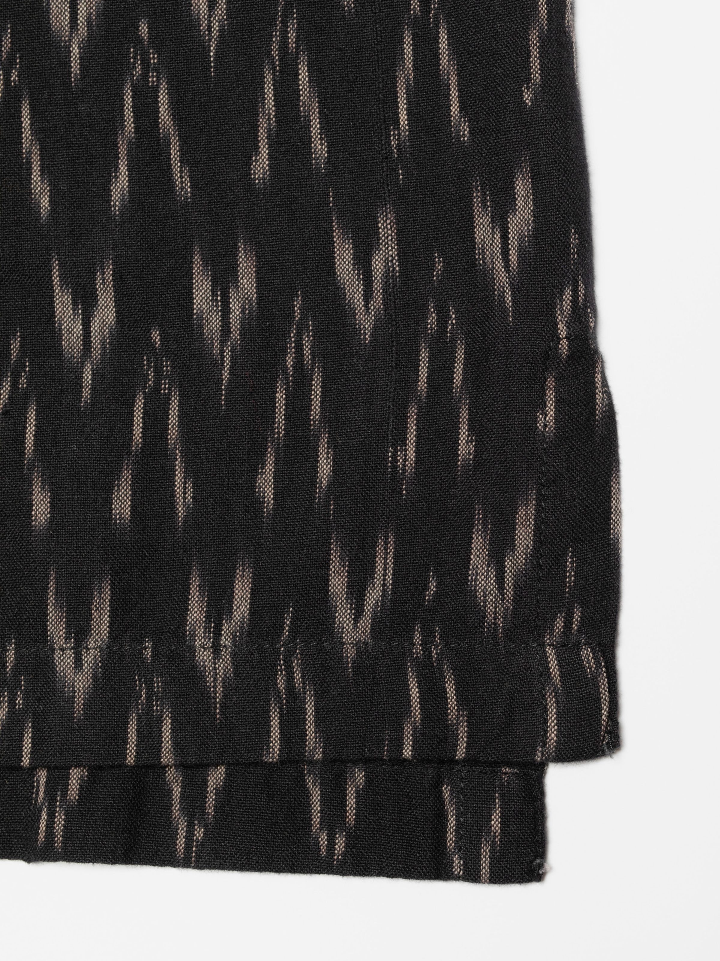 Nudie Jeans Arvid Hawaii Shirt Ikat, close-up of the black organic cotton fabric showing the ikat pattern and hem.