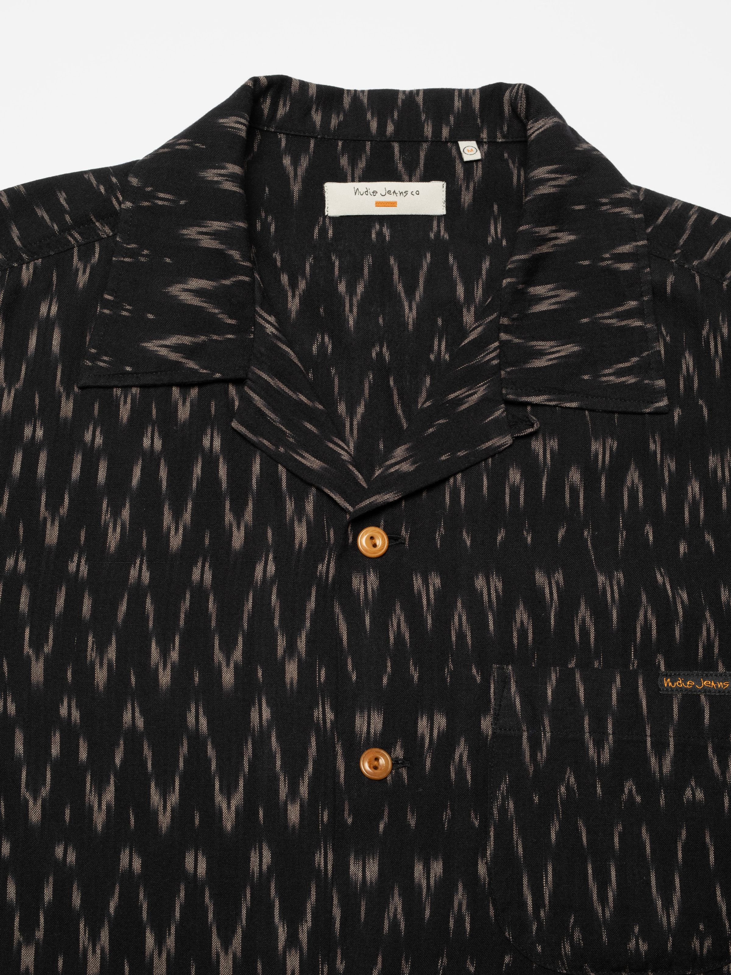 Nudie Jeans Arvid Hawaii Shirt Ikat, close-up showing the camp collar and corozo buttons on the black ikat fabric.