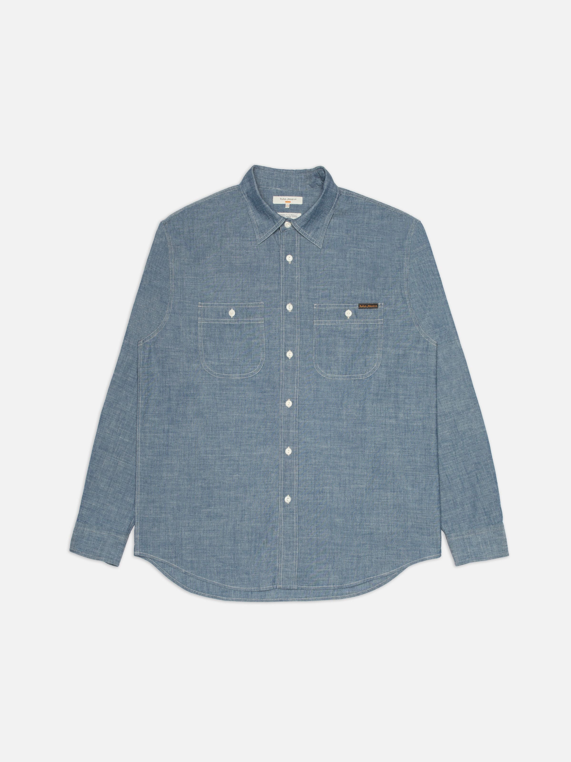 Nudie Jeans Julian Worker Shirt Chambray Blue, ein langärmeliges Hemd aus Bio-Baumwolle mit weißen Nähten, flach liegend.